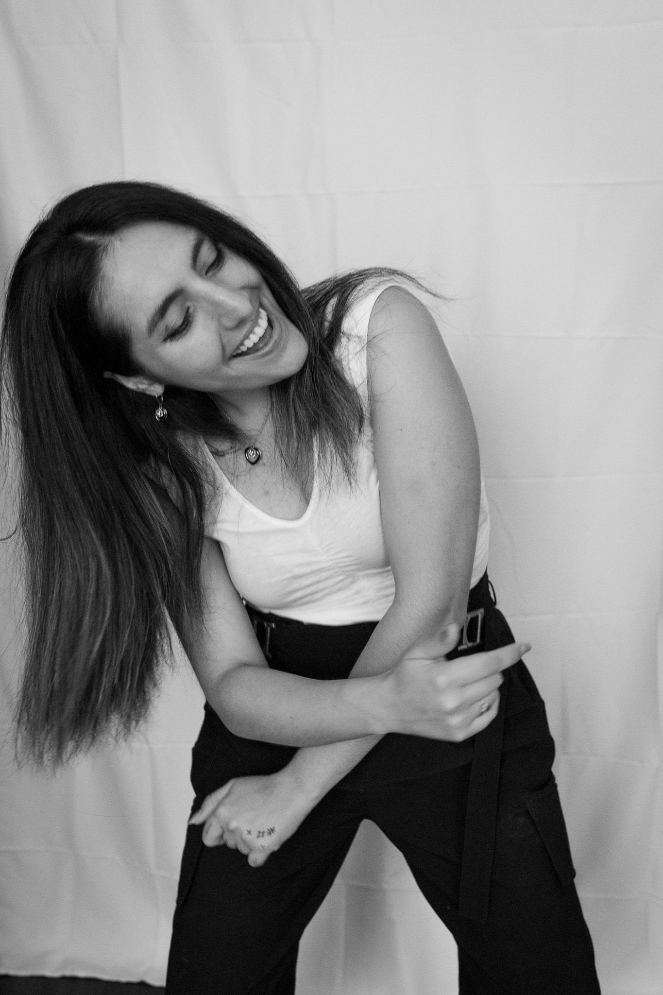 Black and white photo of person in white tank top and dark pants laughing joyfully while dancing against light background.