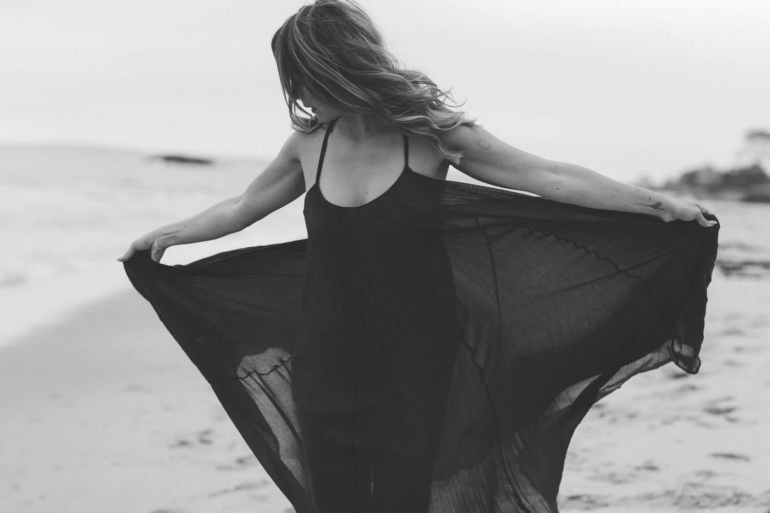 Black and white photo of person spinning with flowing fabric on beach.