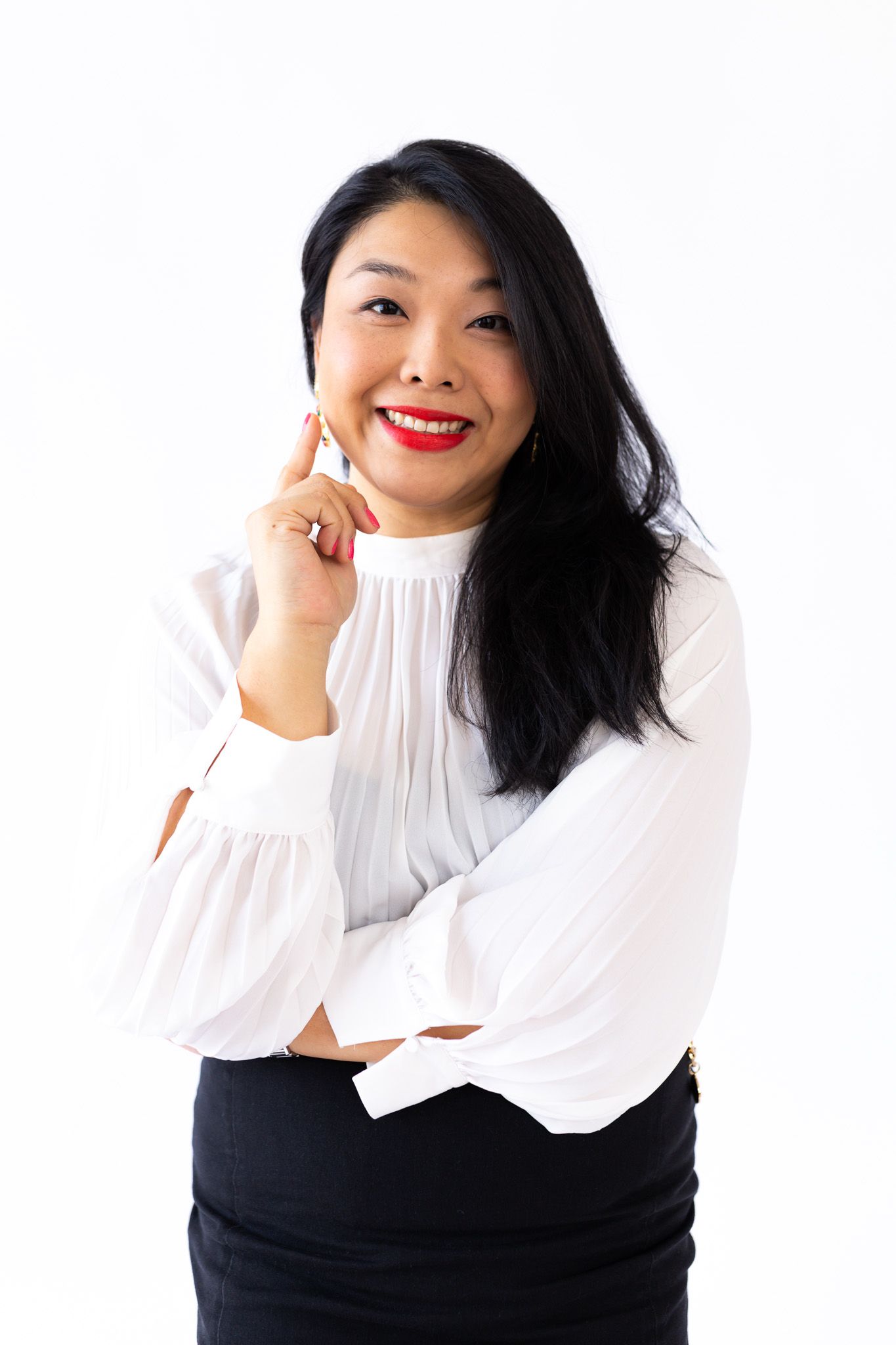Professional portrait of someone wearing a white blouse and black skirt against white background with bright red lipstick.