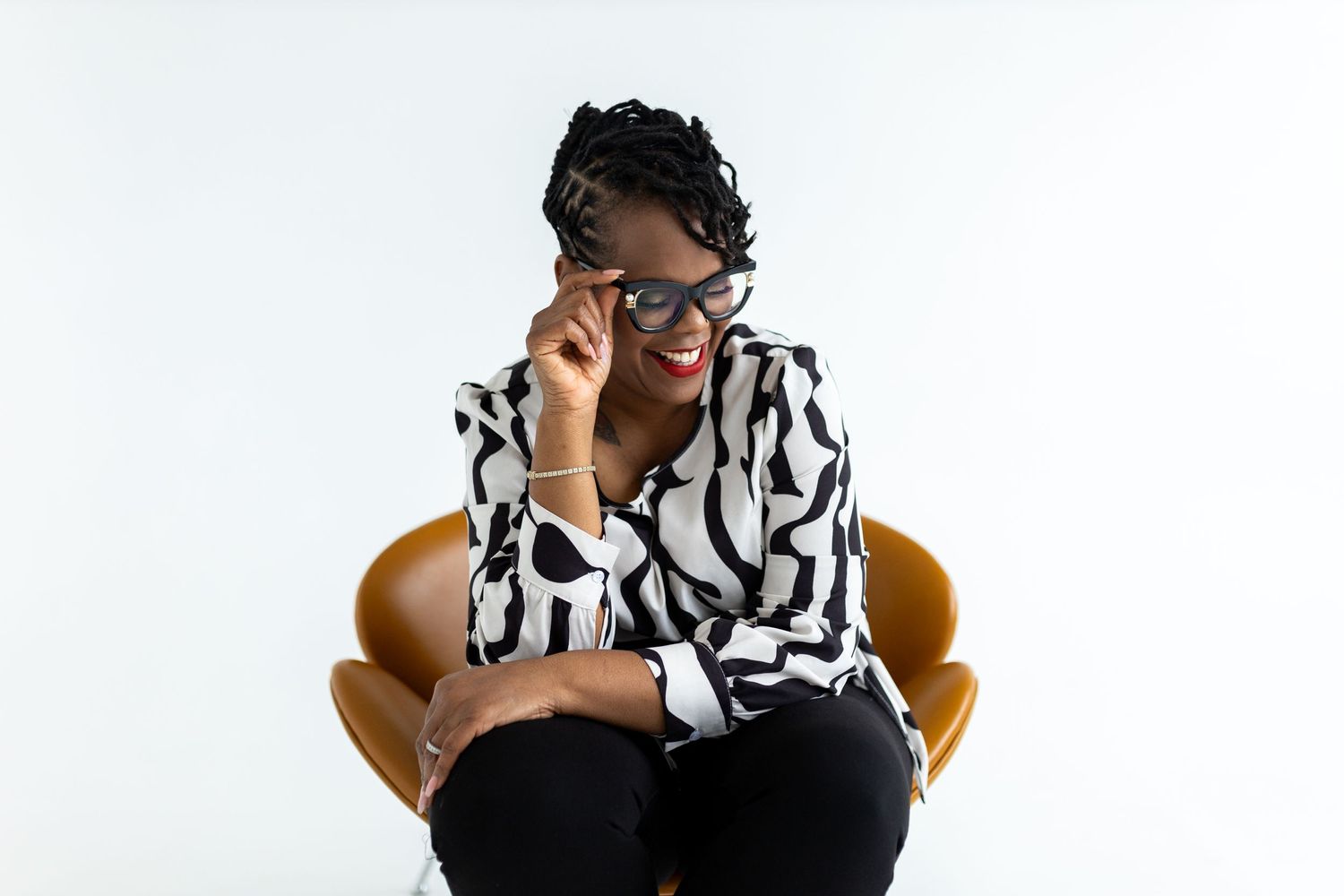 Stylish portrait of person in patterned black and white top seated in orange chair.
