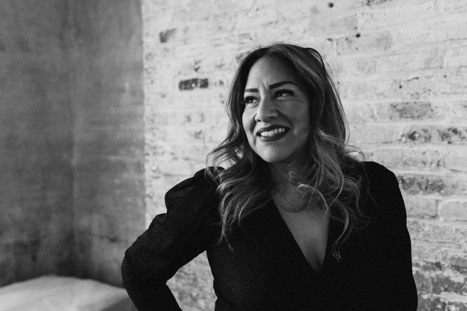 Black and white portrait of someone laughing while wearing dark clothing against a brick wall background.