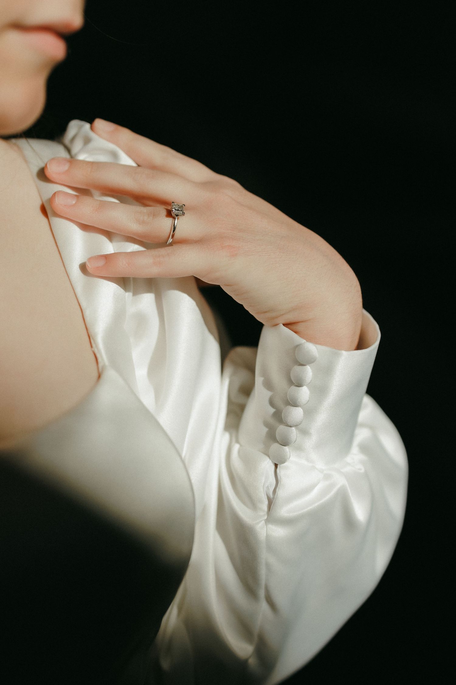 Wedding rings and hands against dark background in artistic lighting.