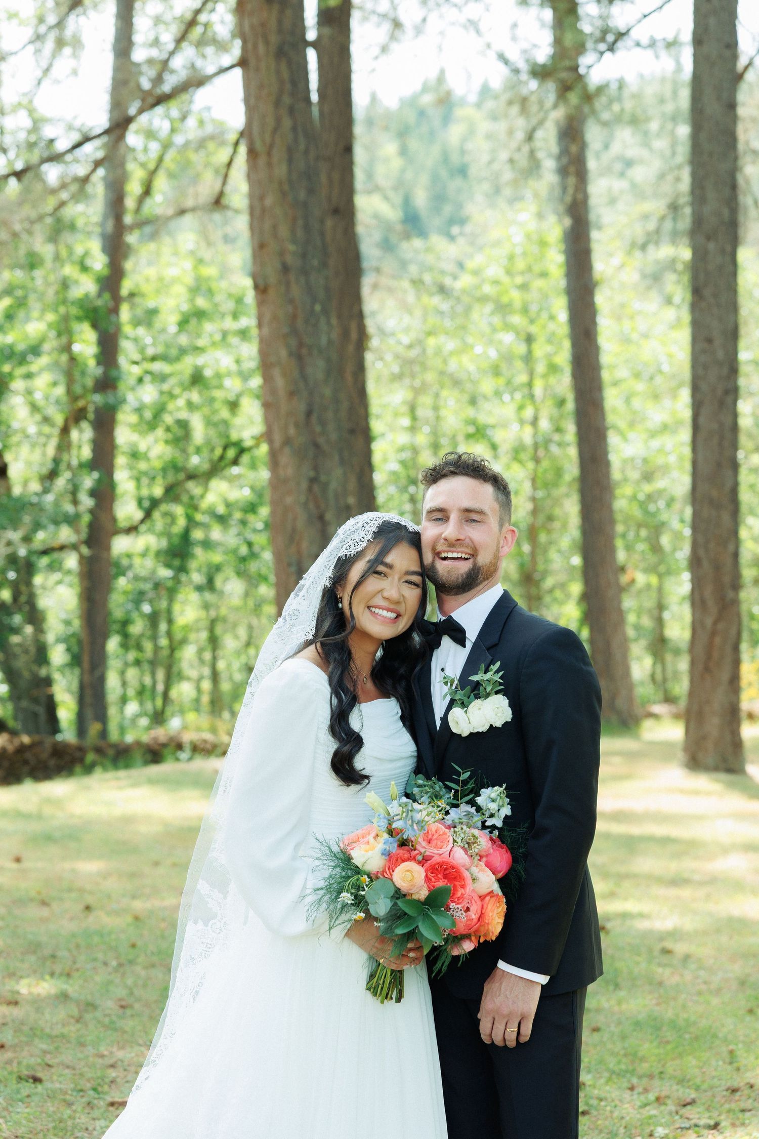 Wedding couple shares joyful moments together in a sunlit forest setting with pine trees in the background.