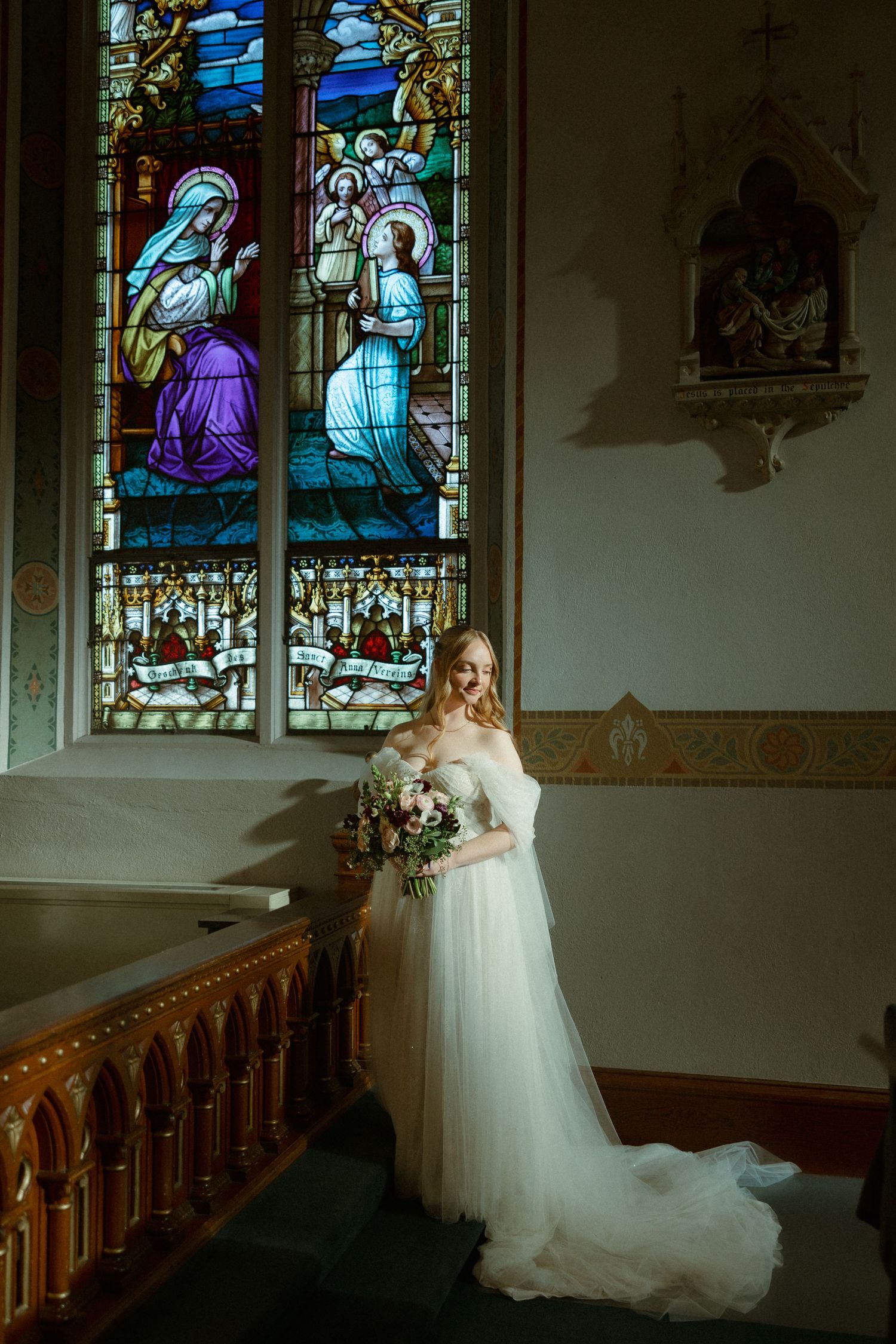 A bride in a flowing white gown poses in front of stained glass windows inside a church sanctuary.