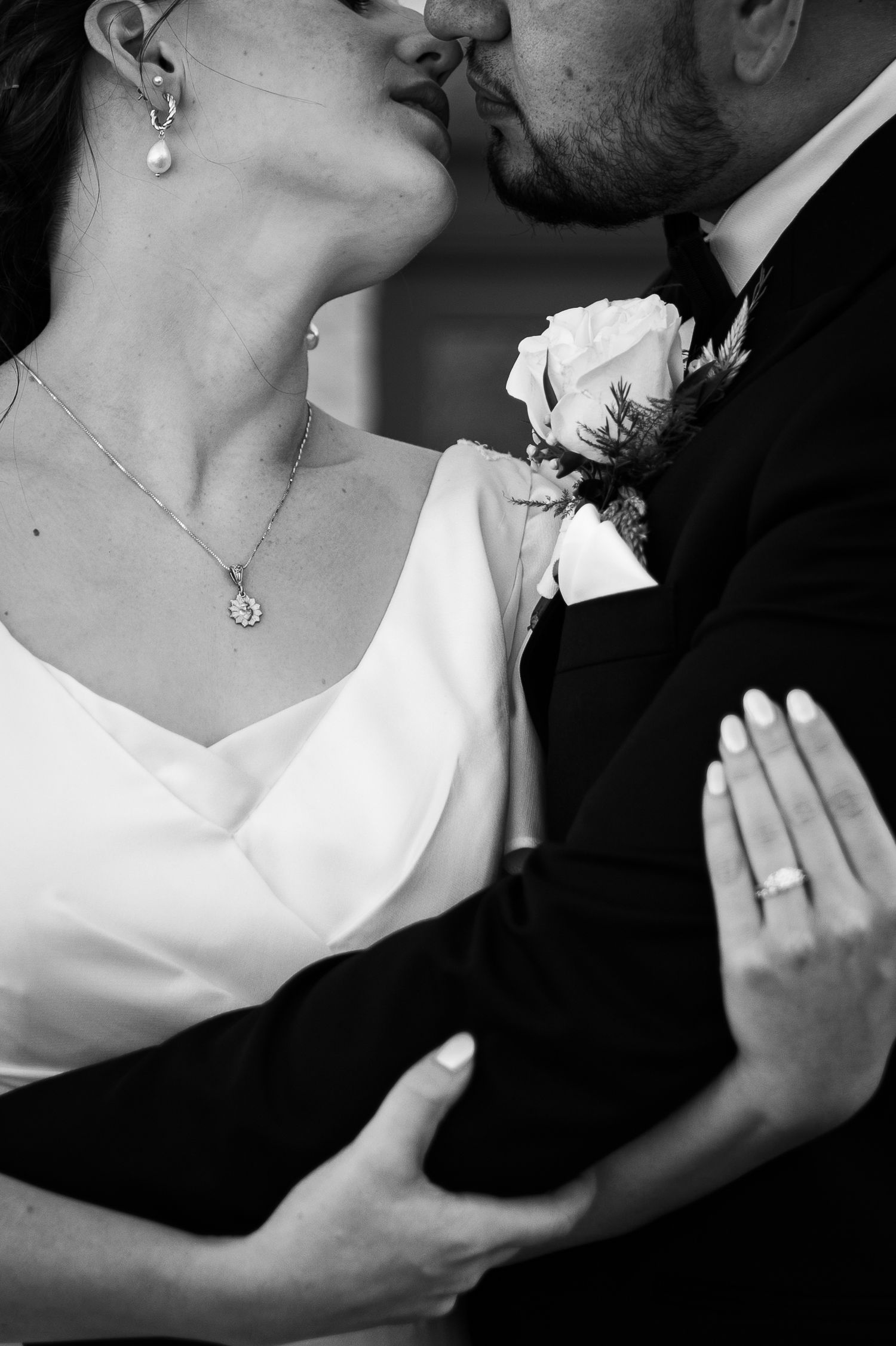 Close-up black and white photo of couple sharing intimate moment with white rose boutonniere.