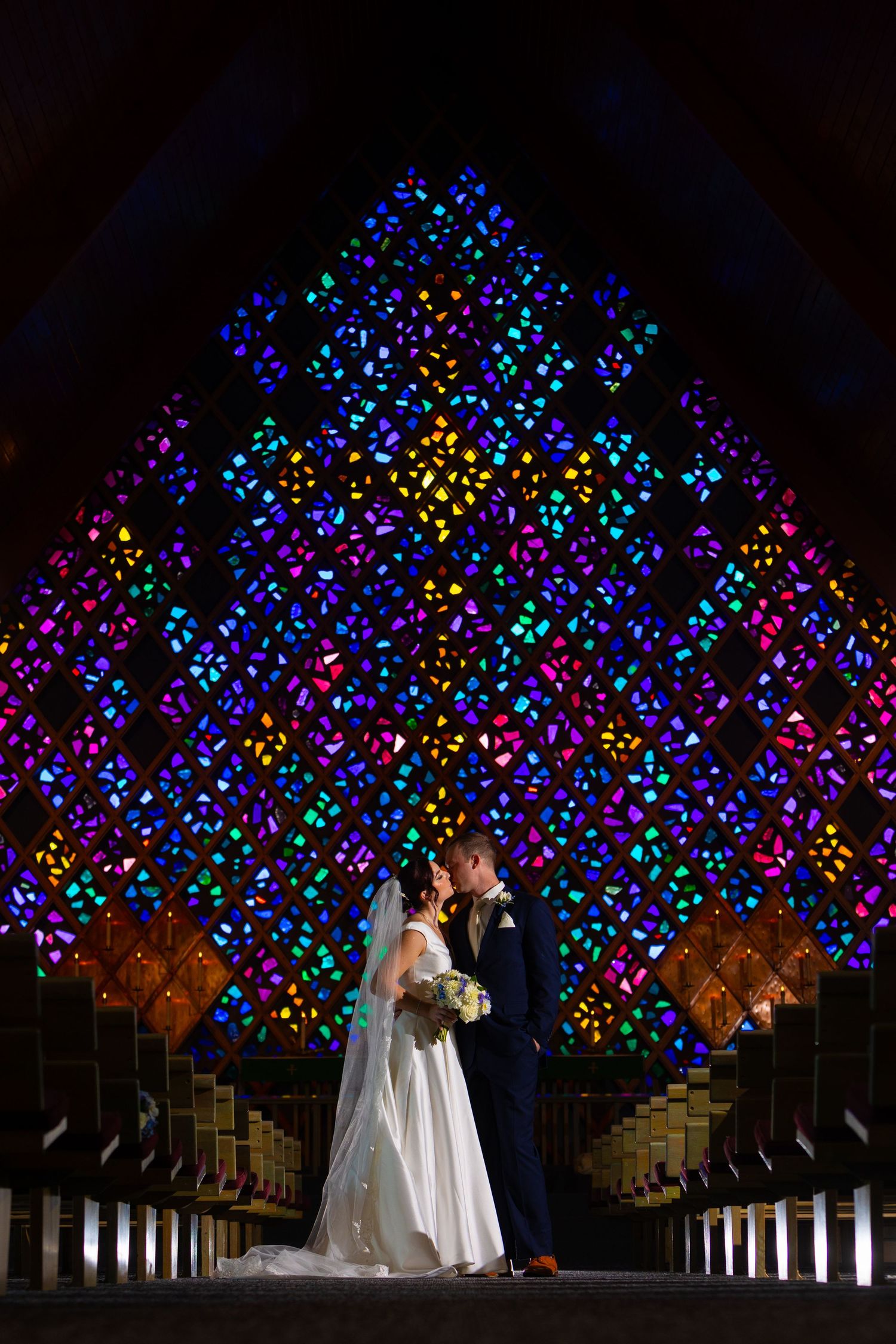 A couple stands beneath a stunning display of colorful butterfly-shaped lights creating a magical nighttime wedding scene.