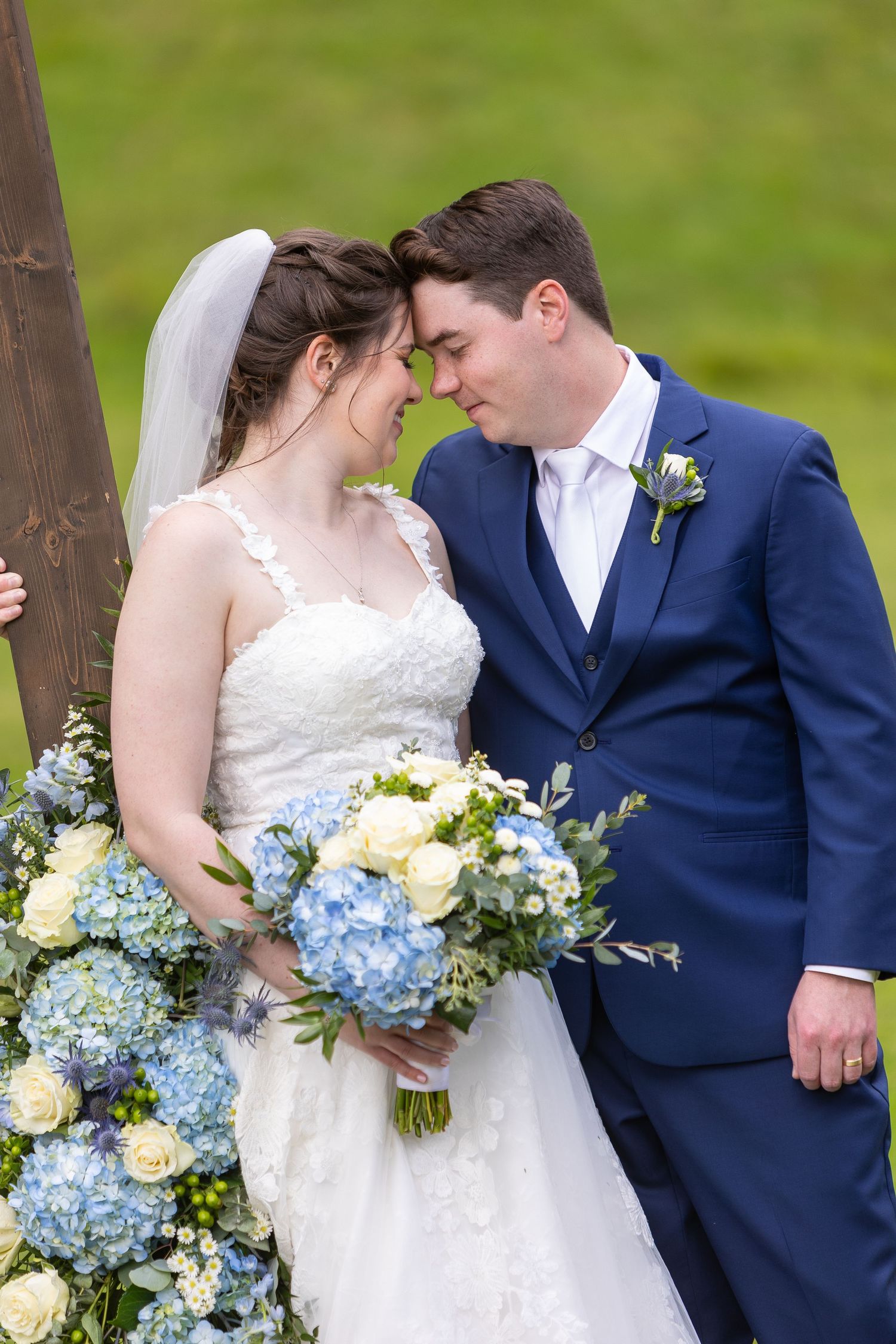 A couple in wedding attire share romantic moments with blue hydrangea and cream rose bouquets.