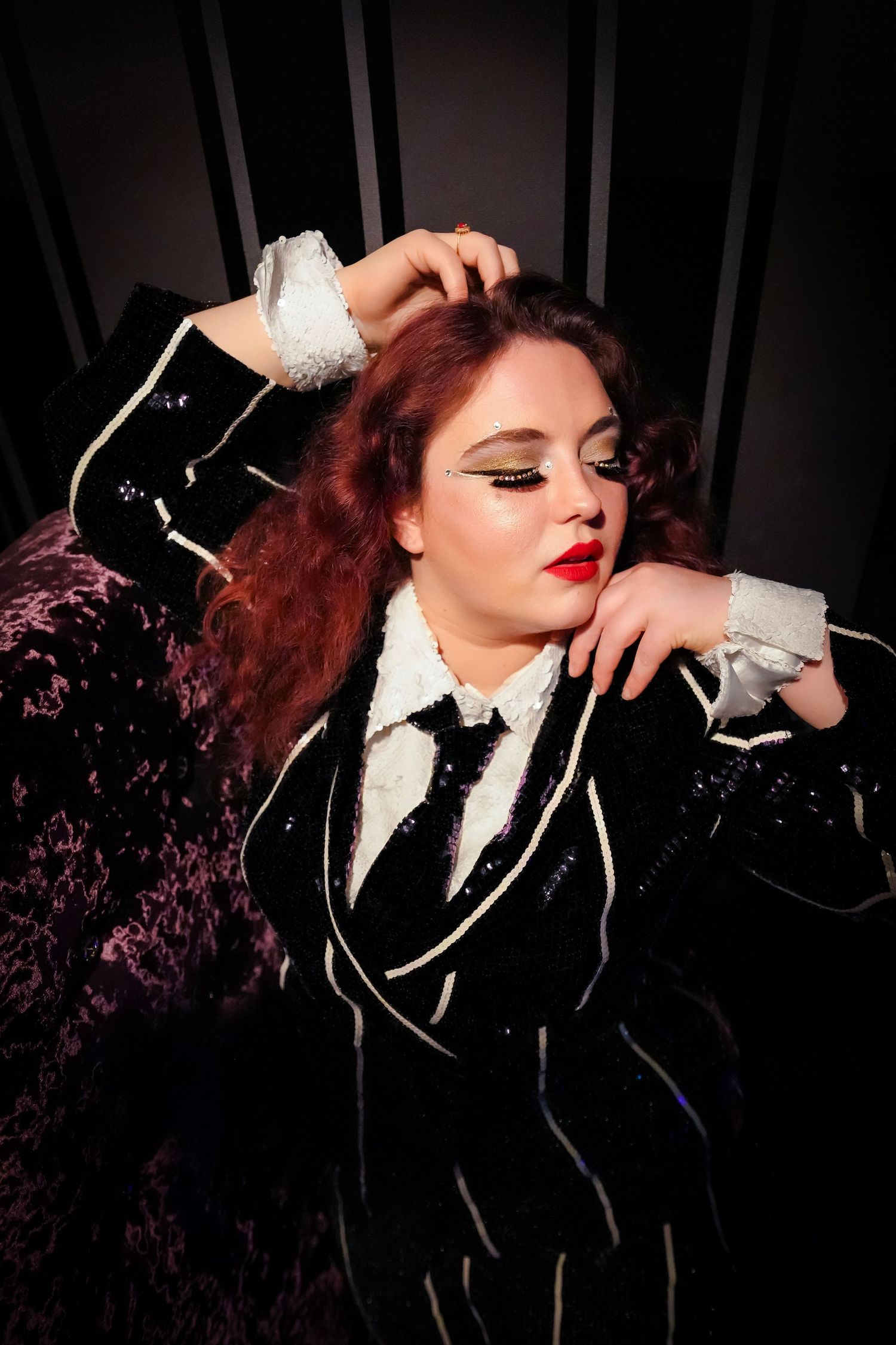Dramatic portrait featuring dark formal attire with white accents, red lipstick, and vintage-inspired styling against dark background.