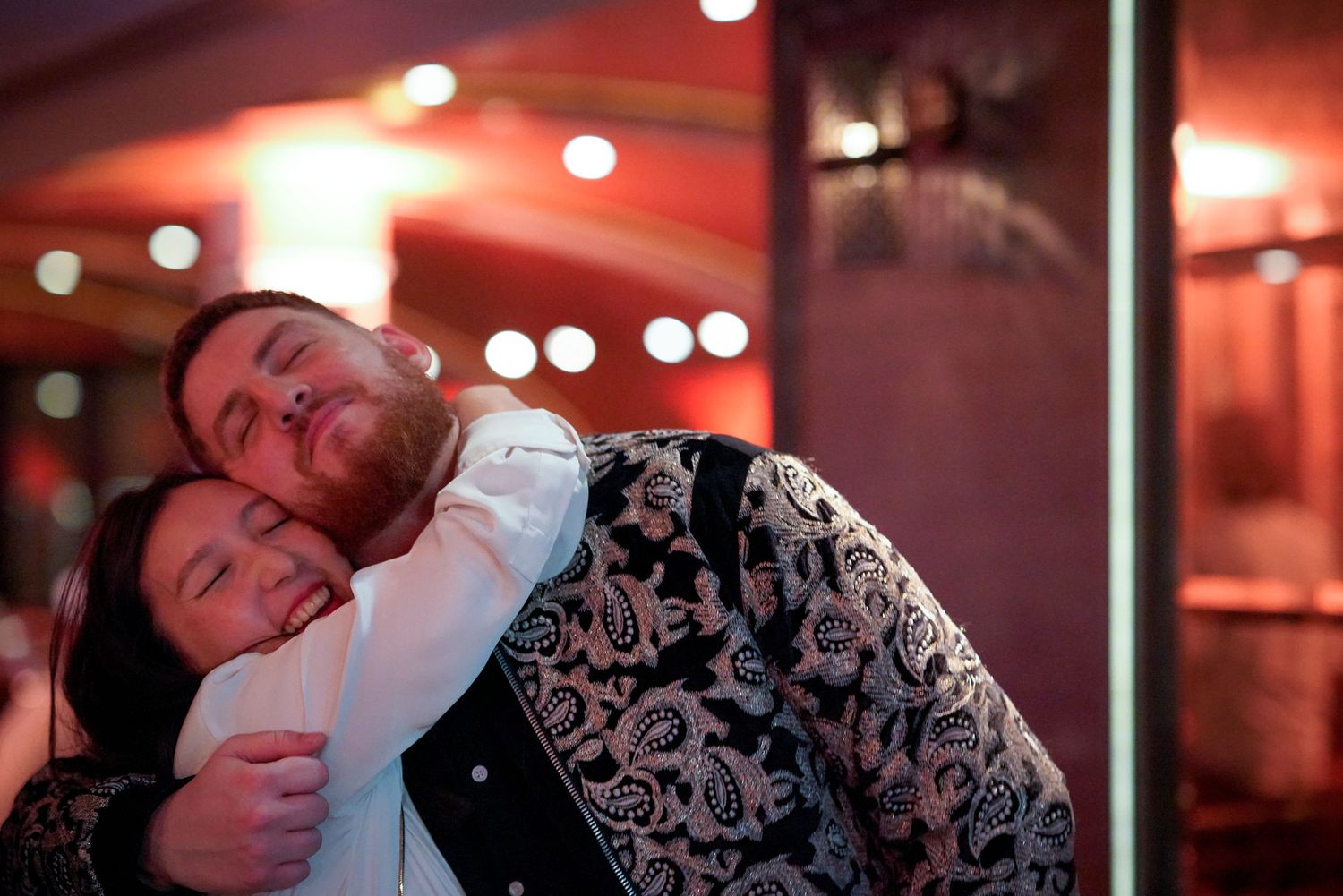 A series of five connected photos showing a couple sharing intimate moments in a dimly lit restaurant setting with red ambient lighting.