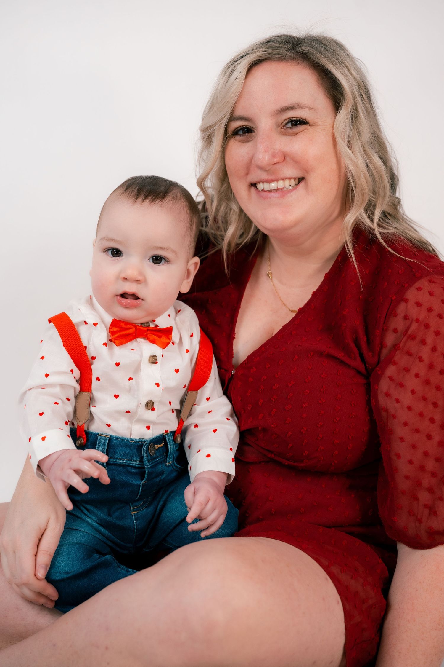 A Valentine's themed portrait of a woman in red holding a baby in heart-print outfit.