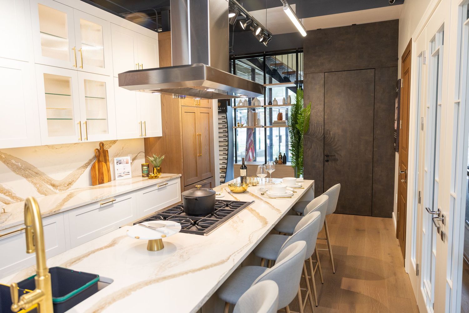 Modern kitchen interior with white marble countertop, stainless steel hood, and bar seating along a sleek peninsula.