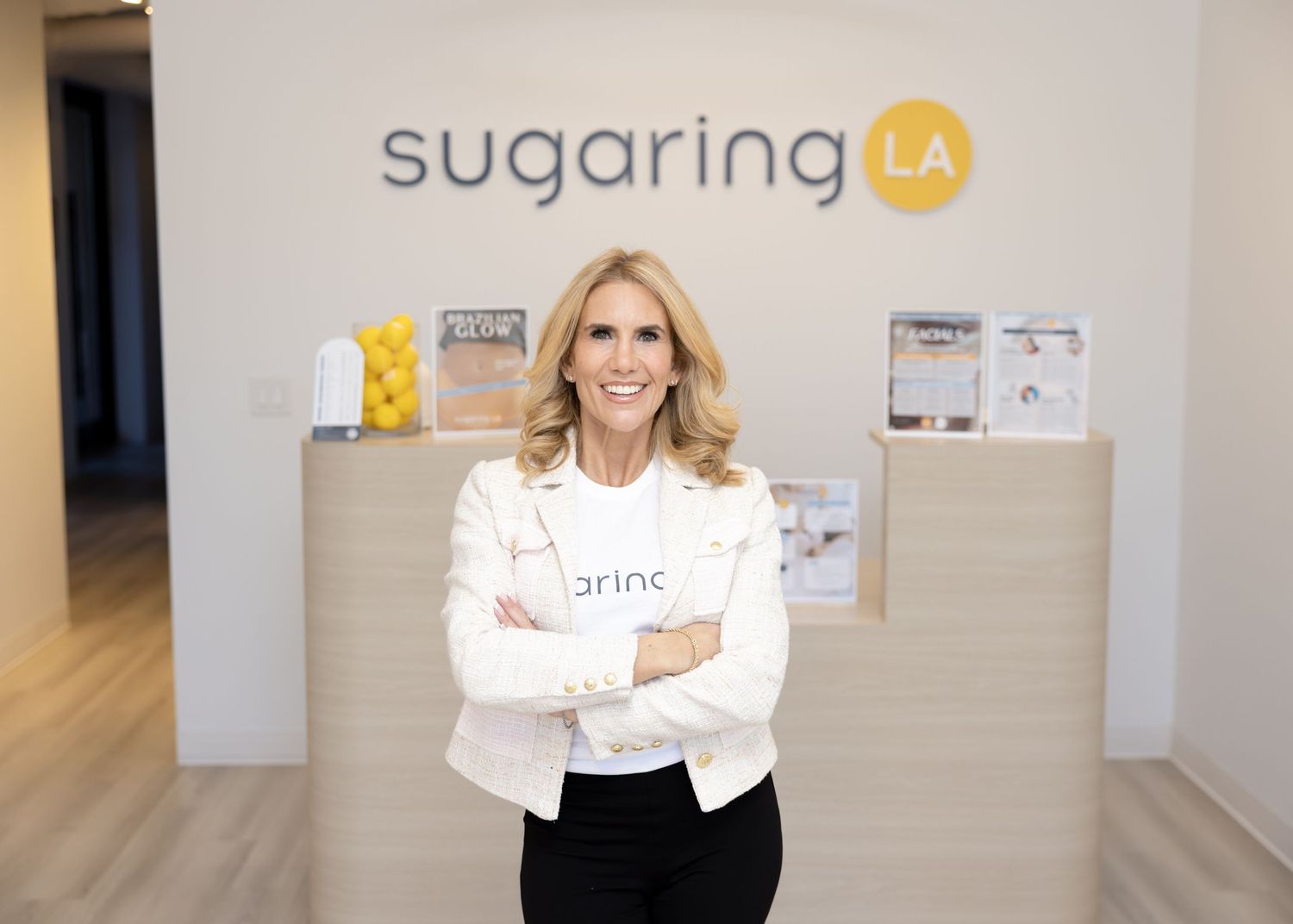 Professional in white blazer stands confidently in front of Sugaring LA business signage.
