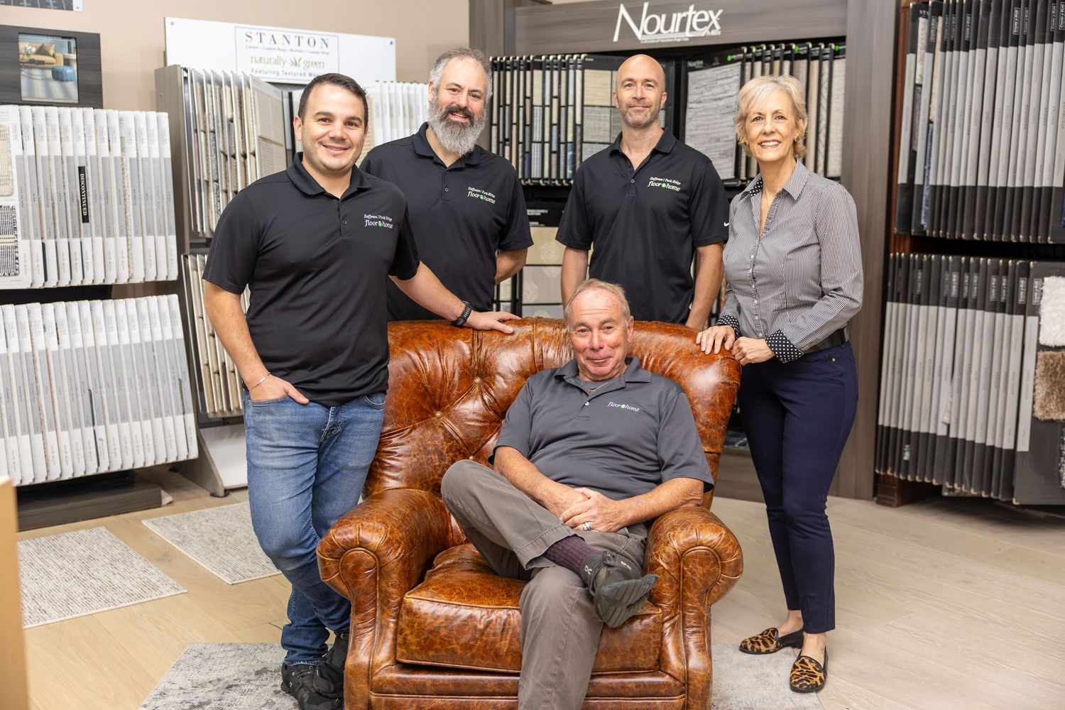Group of people sitting on brown leather couch in a showroom with sample displays visible in background.
