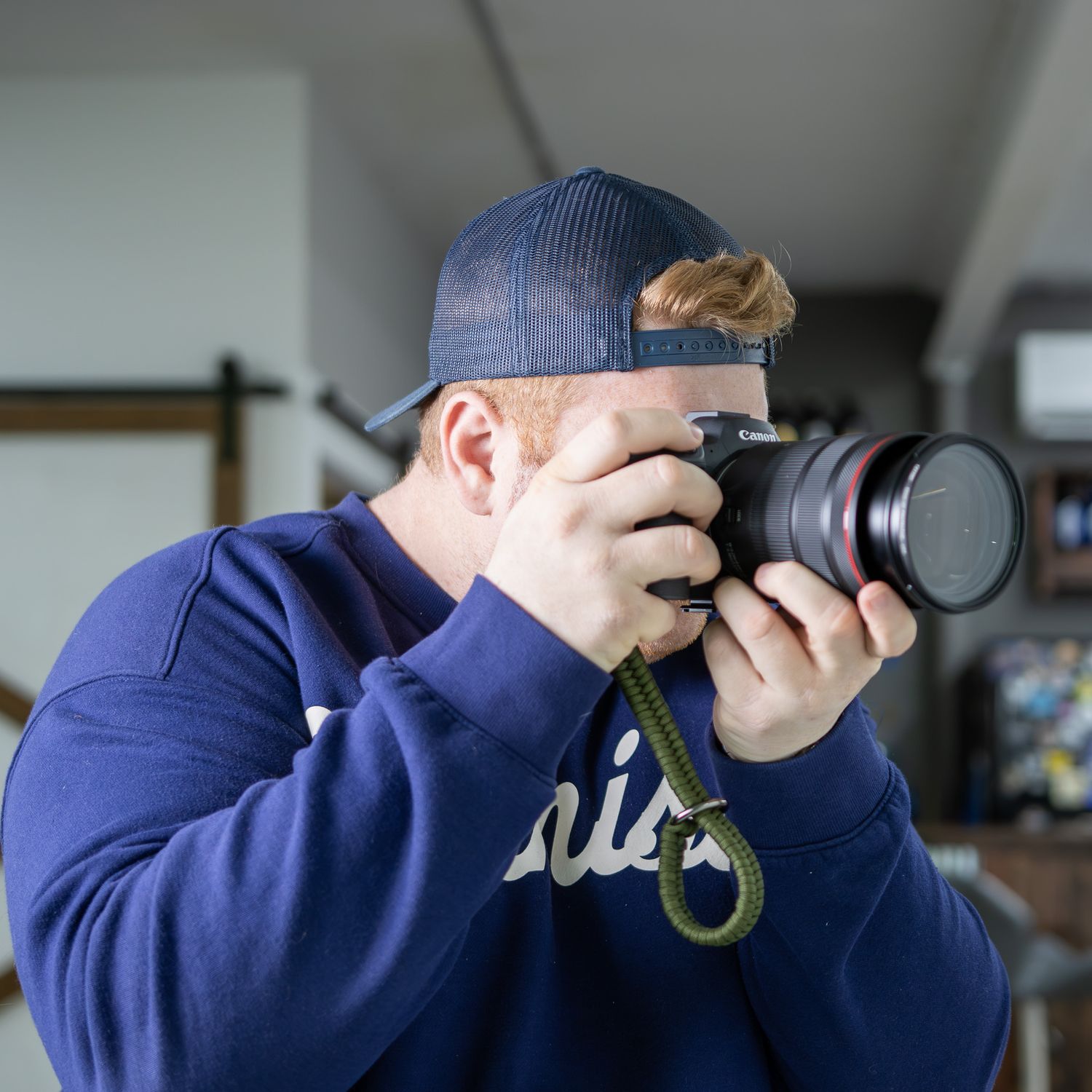 Photographer wearing a blue baseball cap and navy shirt takes a photo with a professional camera and telephoto lens.