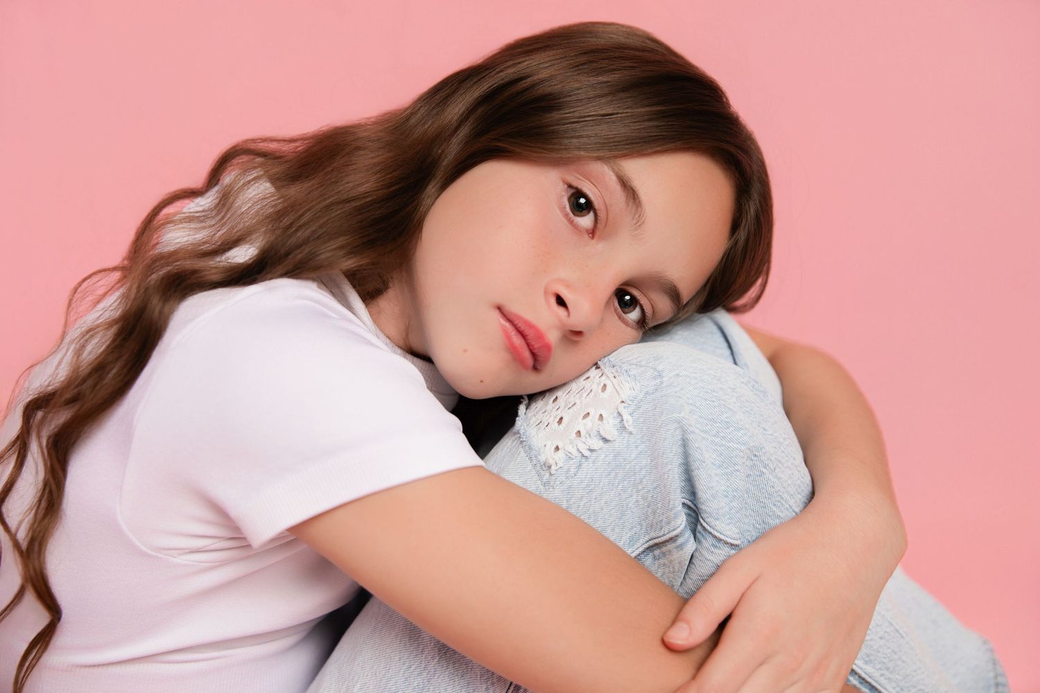 Young person with long brown hair wearing gray casual wear laying on pink background.