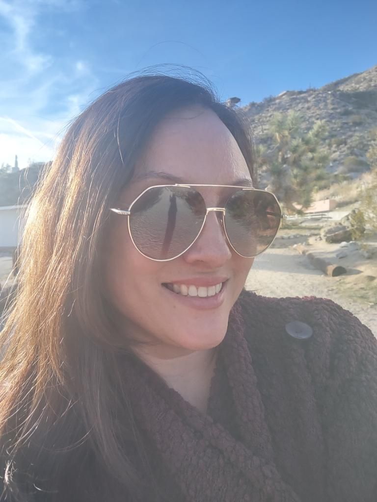 Person wearing aviator sunglasses and winter coat smiles during sunny mountain day.