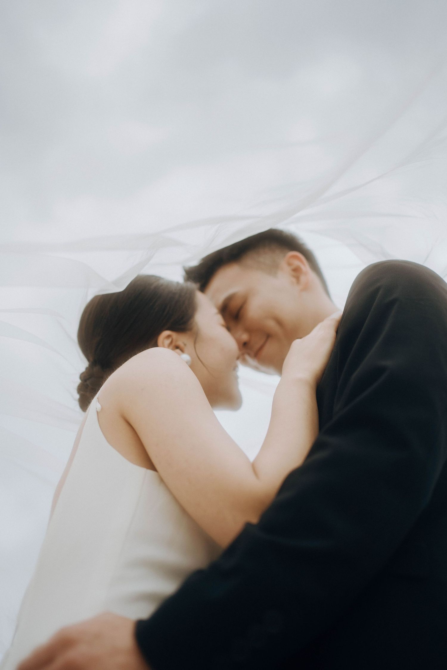 A tender romantic moment captured between a couple in formal attire against a soft cloudy sky.