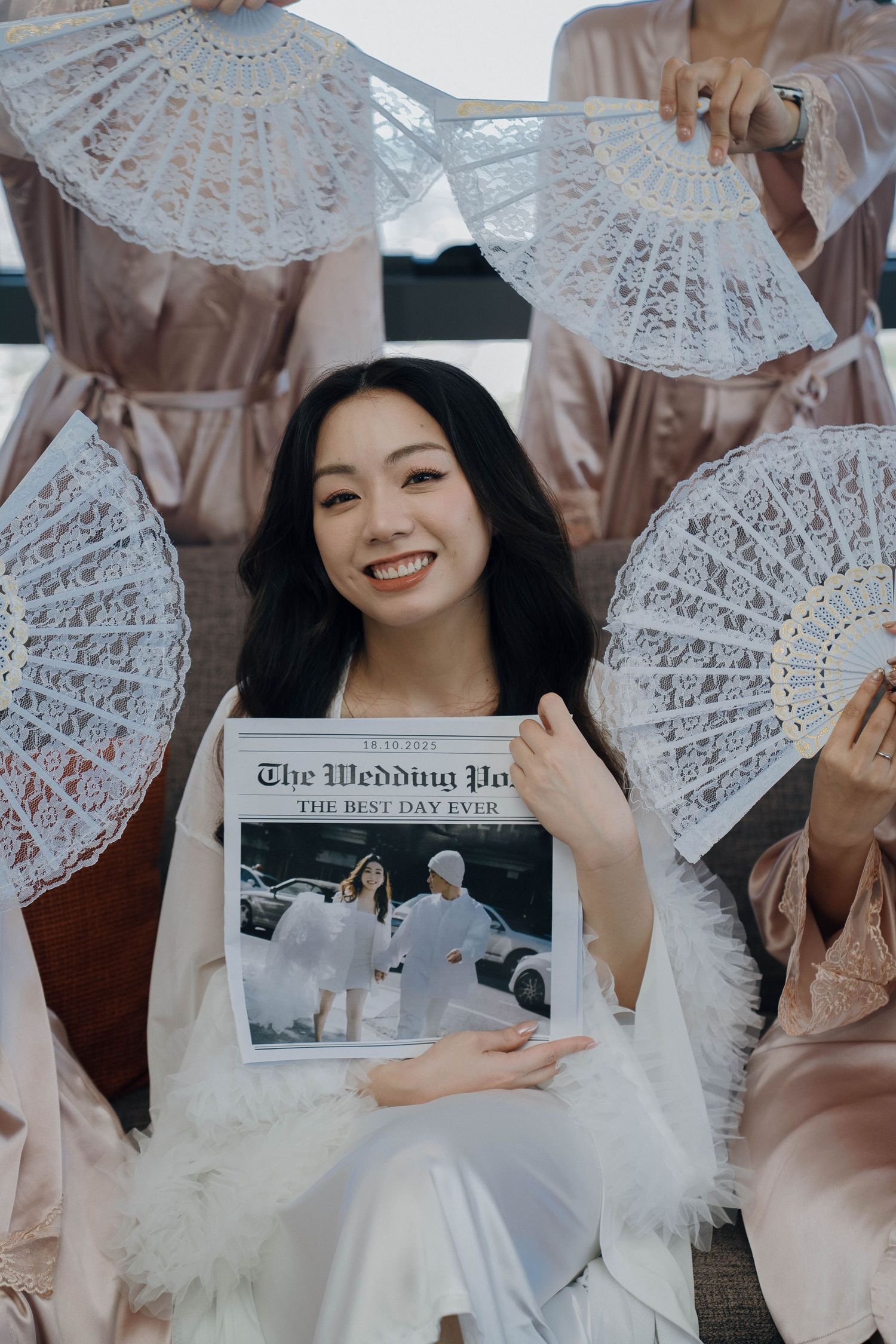 Bridesmaids in blush pink dresses pose with delicate white lace parasols during an elegant wedding photoshoot.