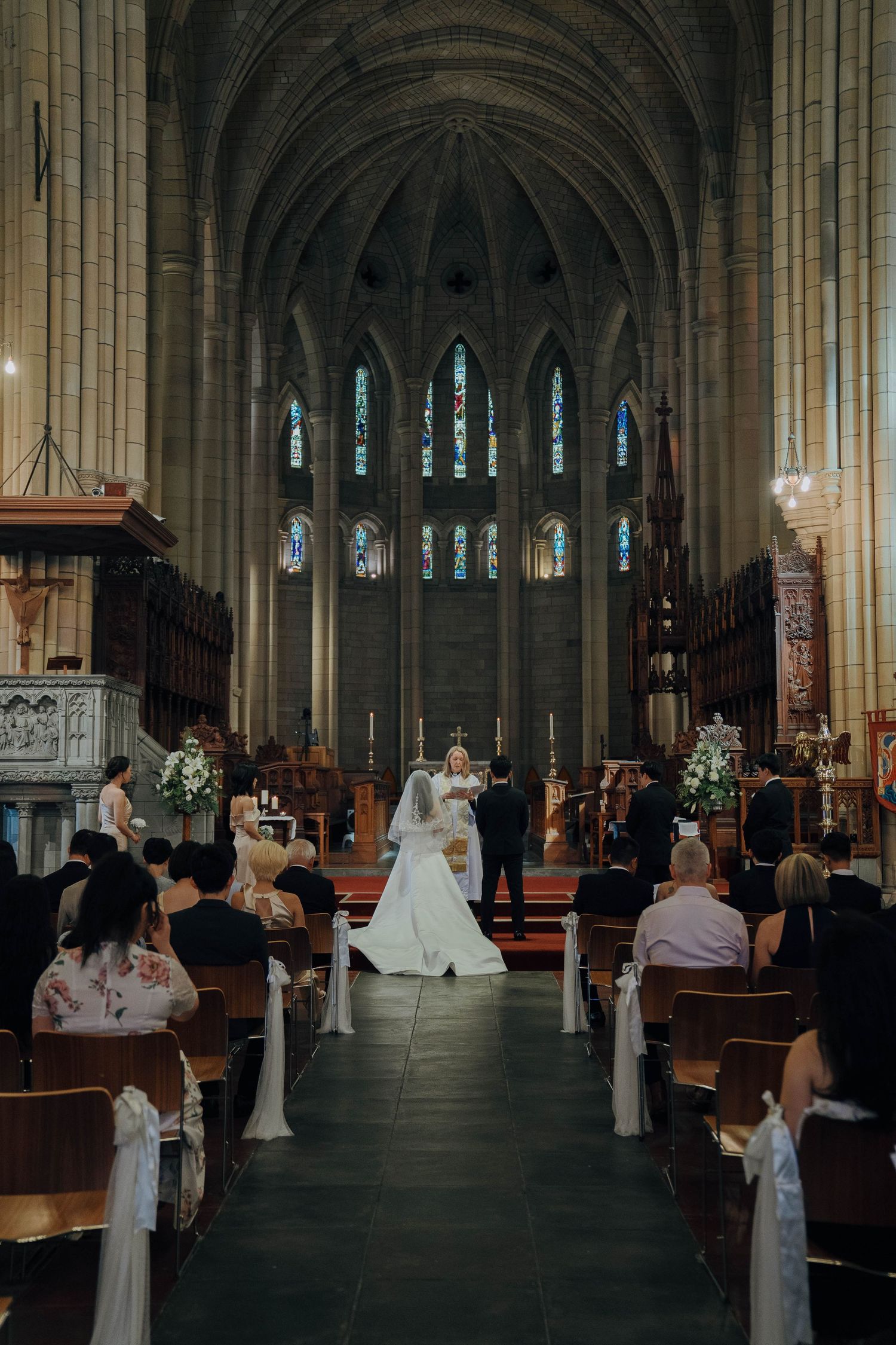 Wedding ceremony taking place inside a grand Gothic cathedral with soaring columns and stained glass windows.