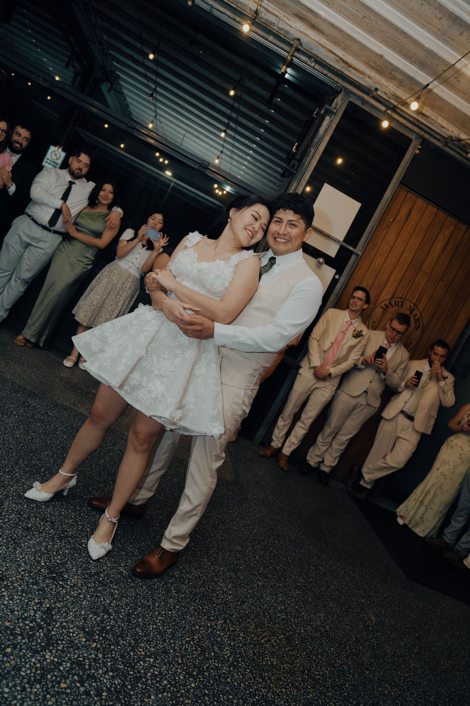 Wedding guests gather around to watch a couple dance during the garter toss tradition at an indoor reception venue.