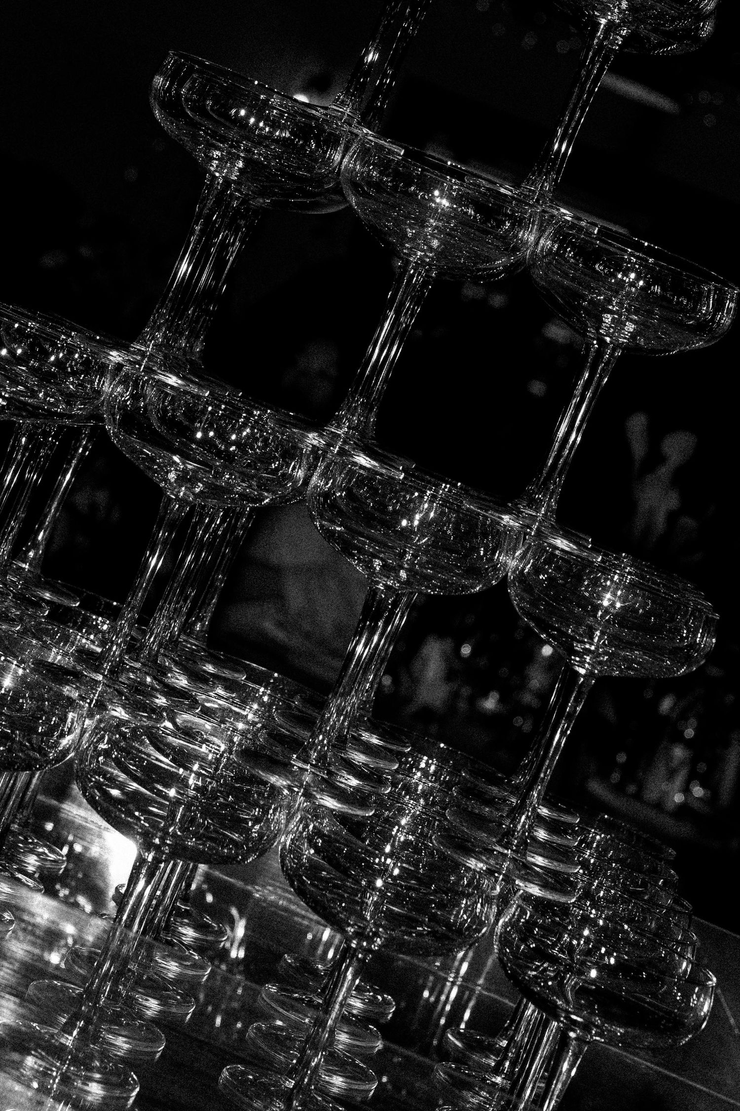 A dramatic black and white photo of empty champagne glasses stacked in a pyramid formation, reflecting light and shadows.