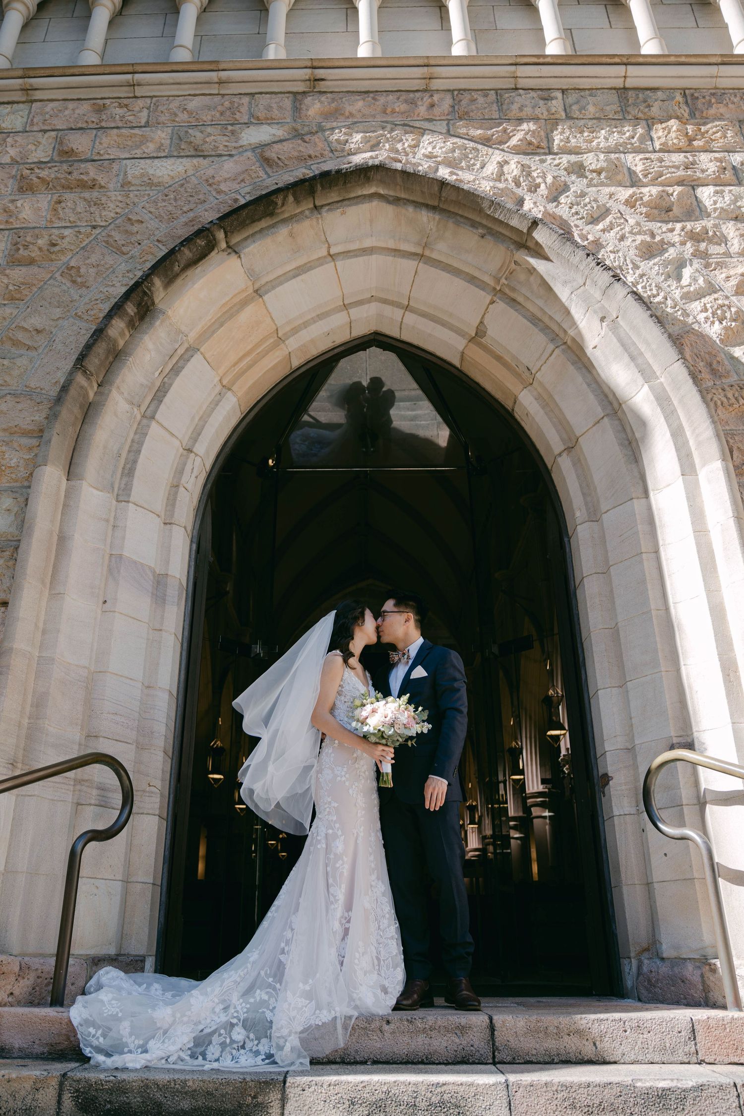 A couple shares a romantic moment under a grand stone archway entrance of a church on their wedding day.