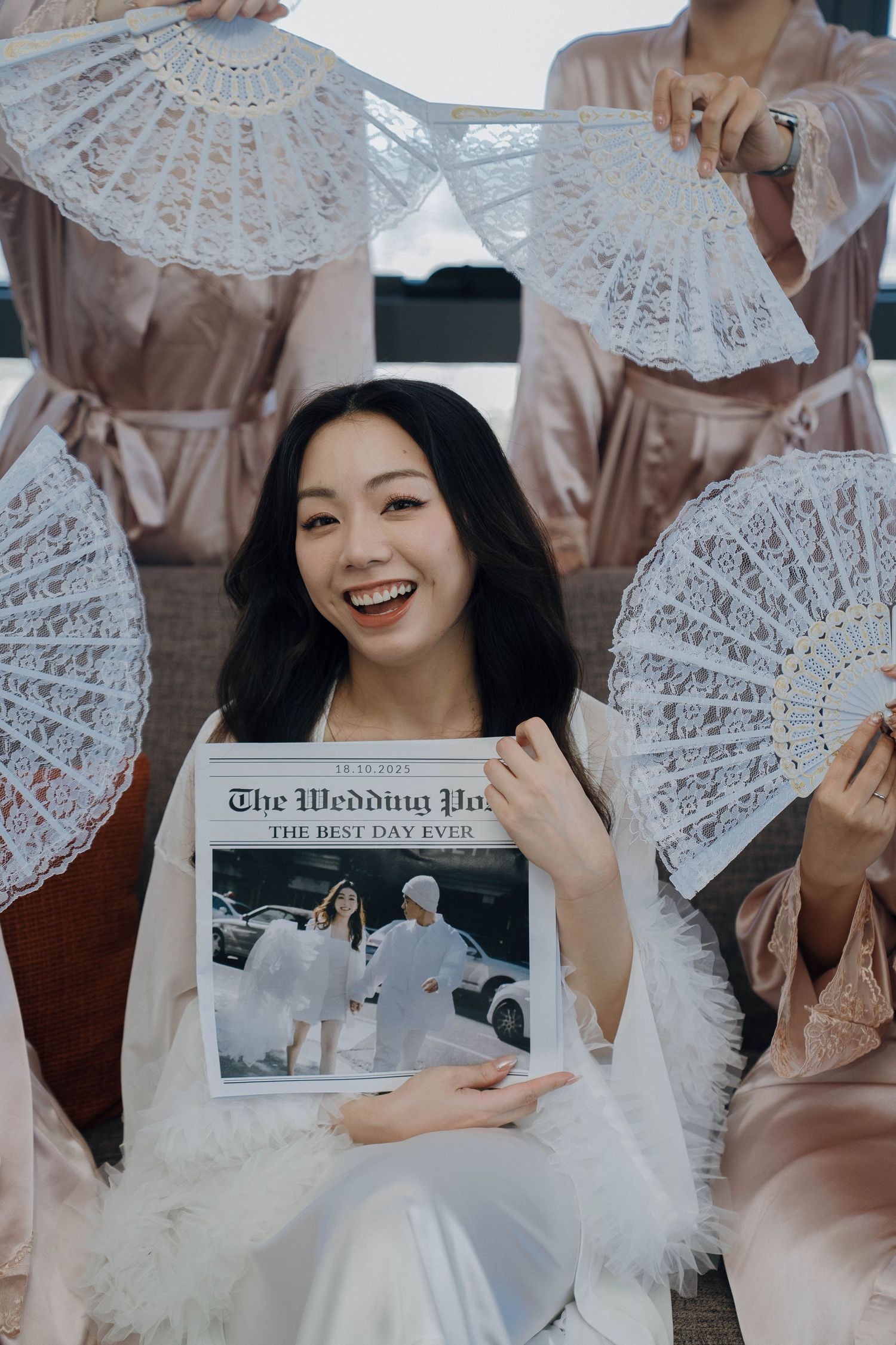 Someone in white holds a wedding newspaper while surrounded by decorative white lace fans in an elegant photo setting.