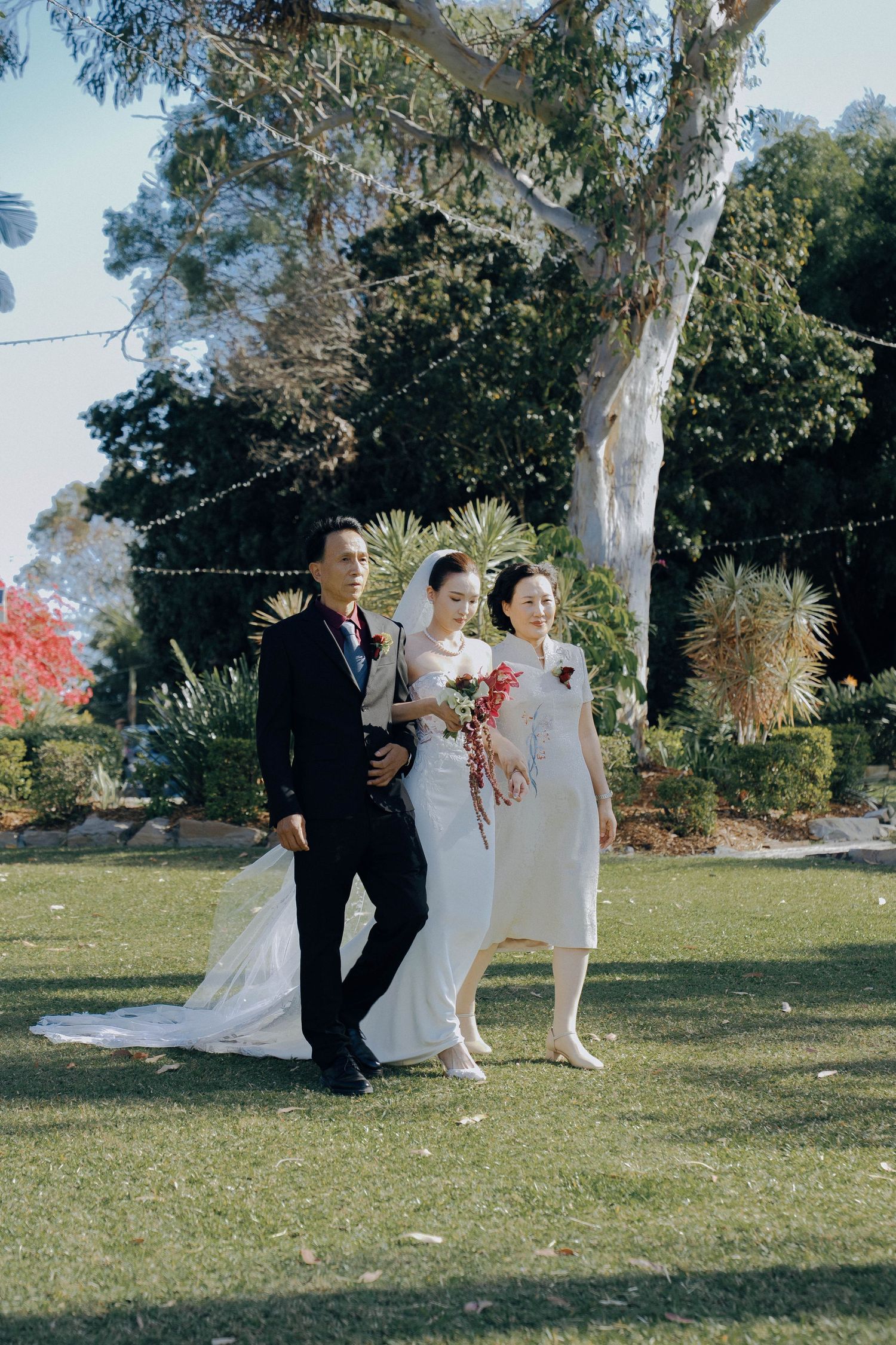 Wedding party members walk together on a sunny lawn during an outdoor celebration.