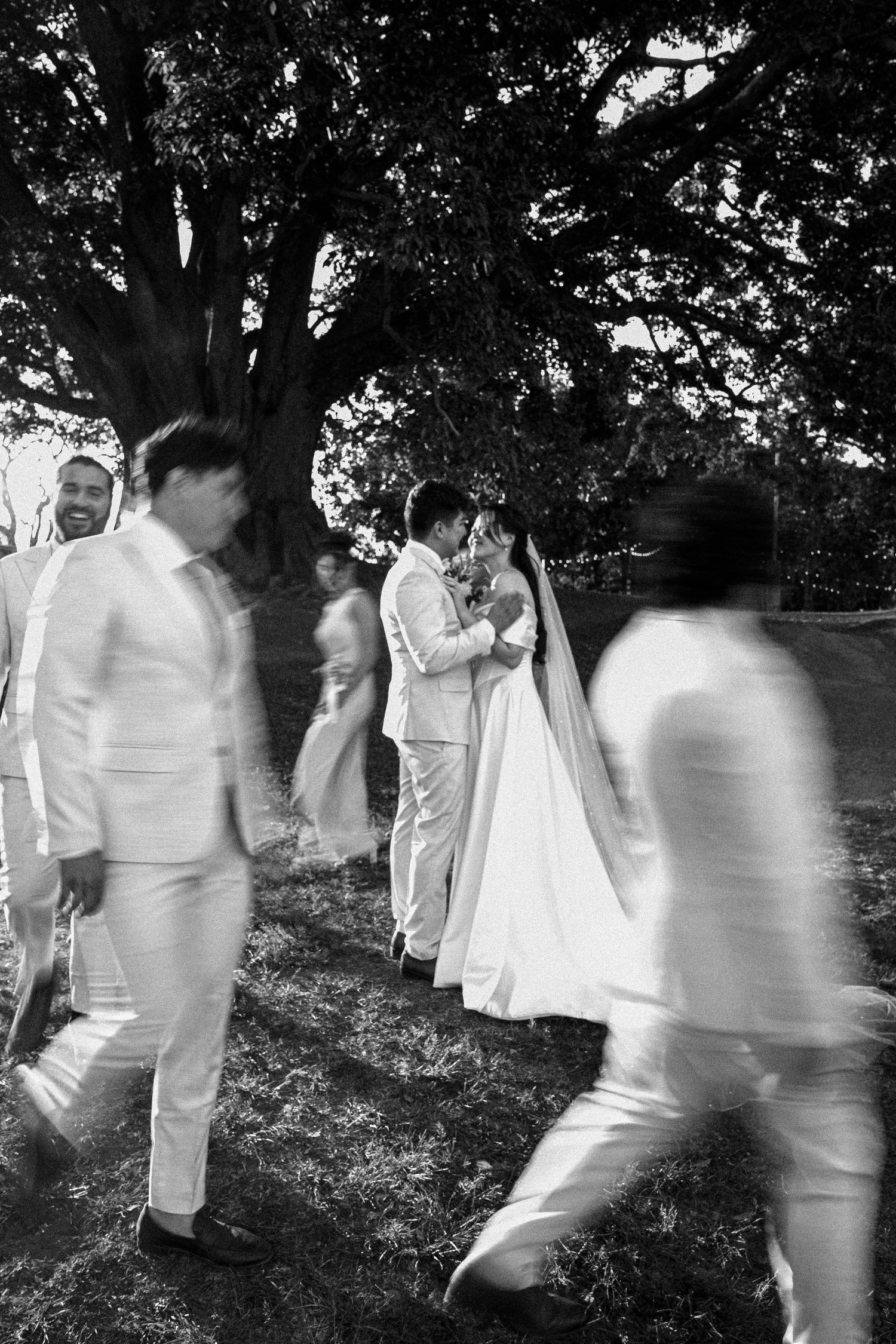 A series of blurred black and white photographs showing people in white clothing moving through a wooded area.
