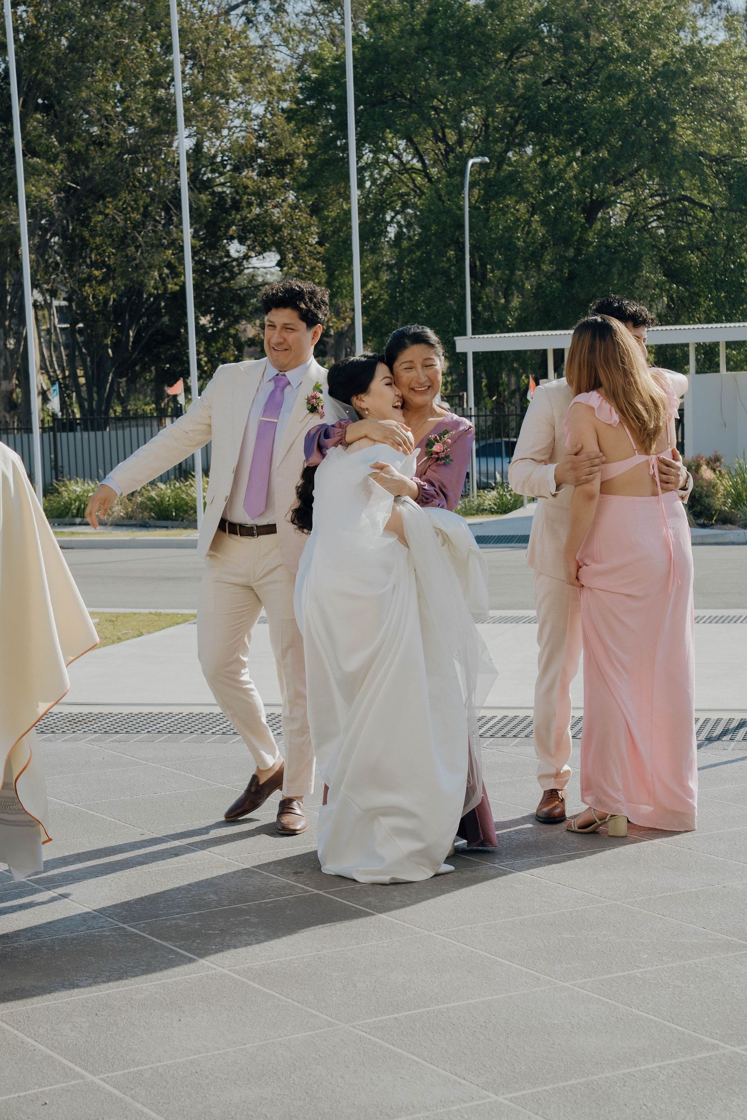 Wedding party in pink and white attire sits on modern concrete steps during an outdoor photo session.