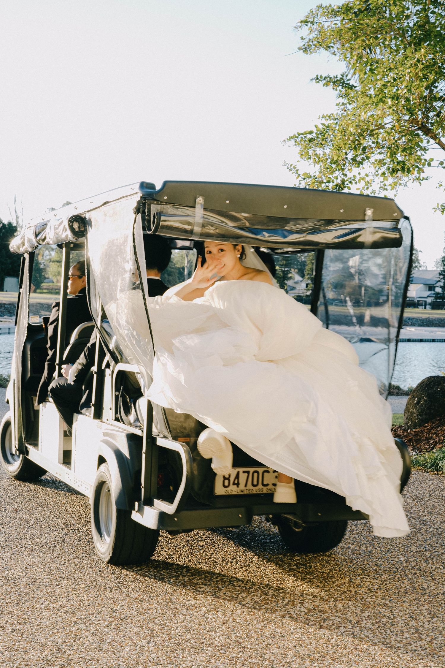 White wedding dress flowing out of a classic car door parked on gravel.