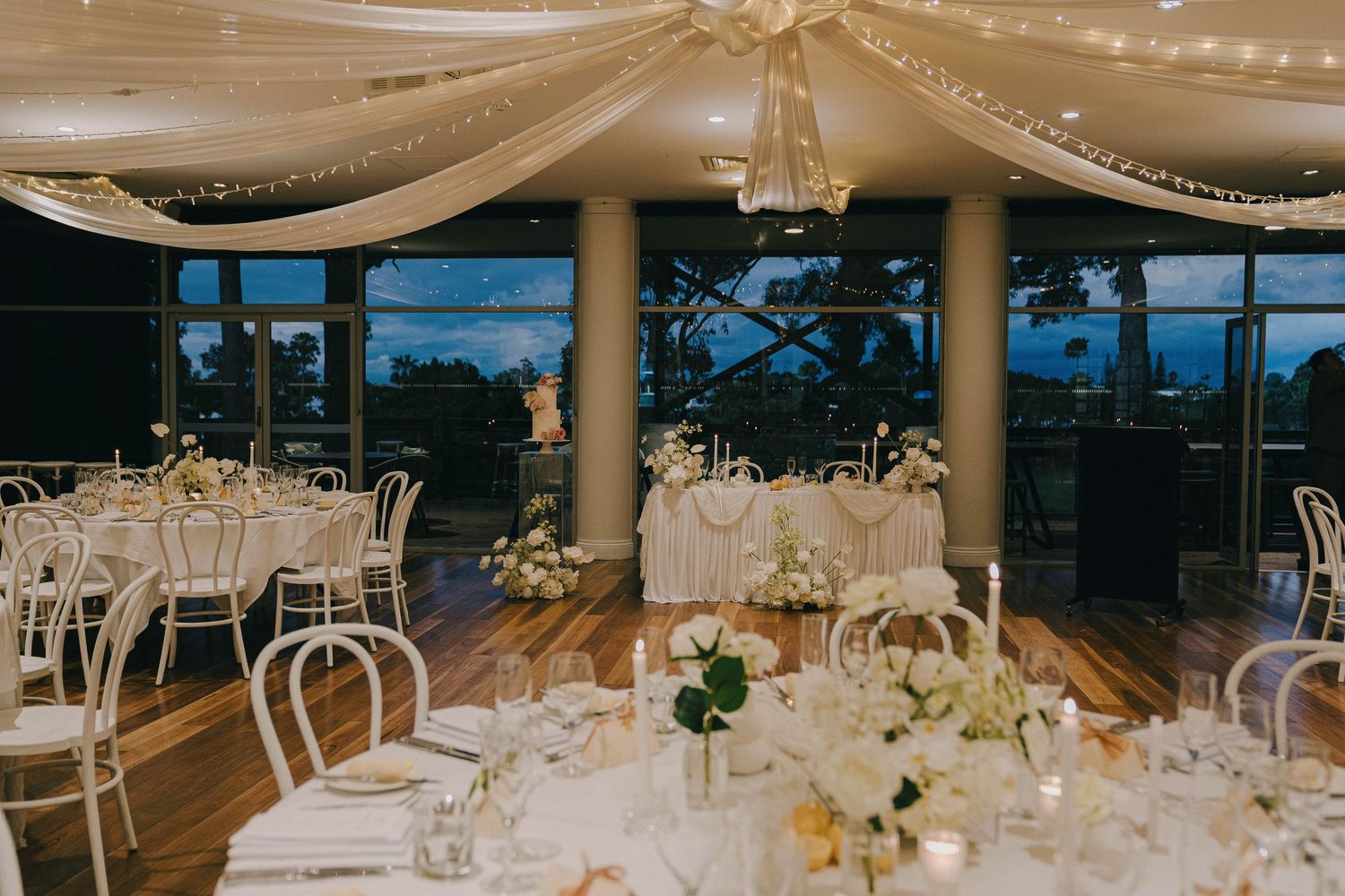 Elegant wedding reception venue with draped white fabric ceiling, crystal chandeliers and round dining tables.