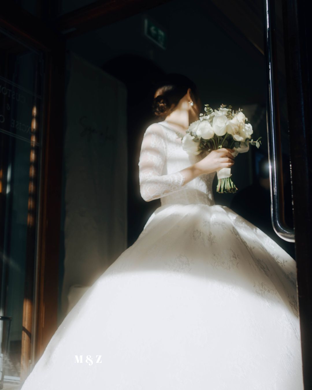 A bride in a white winter wedding dress with fur trim holds a bouquet of white roses in a dimly lit setting.