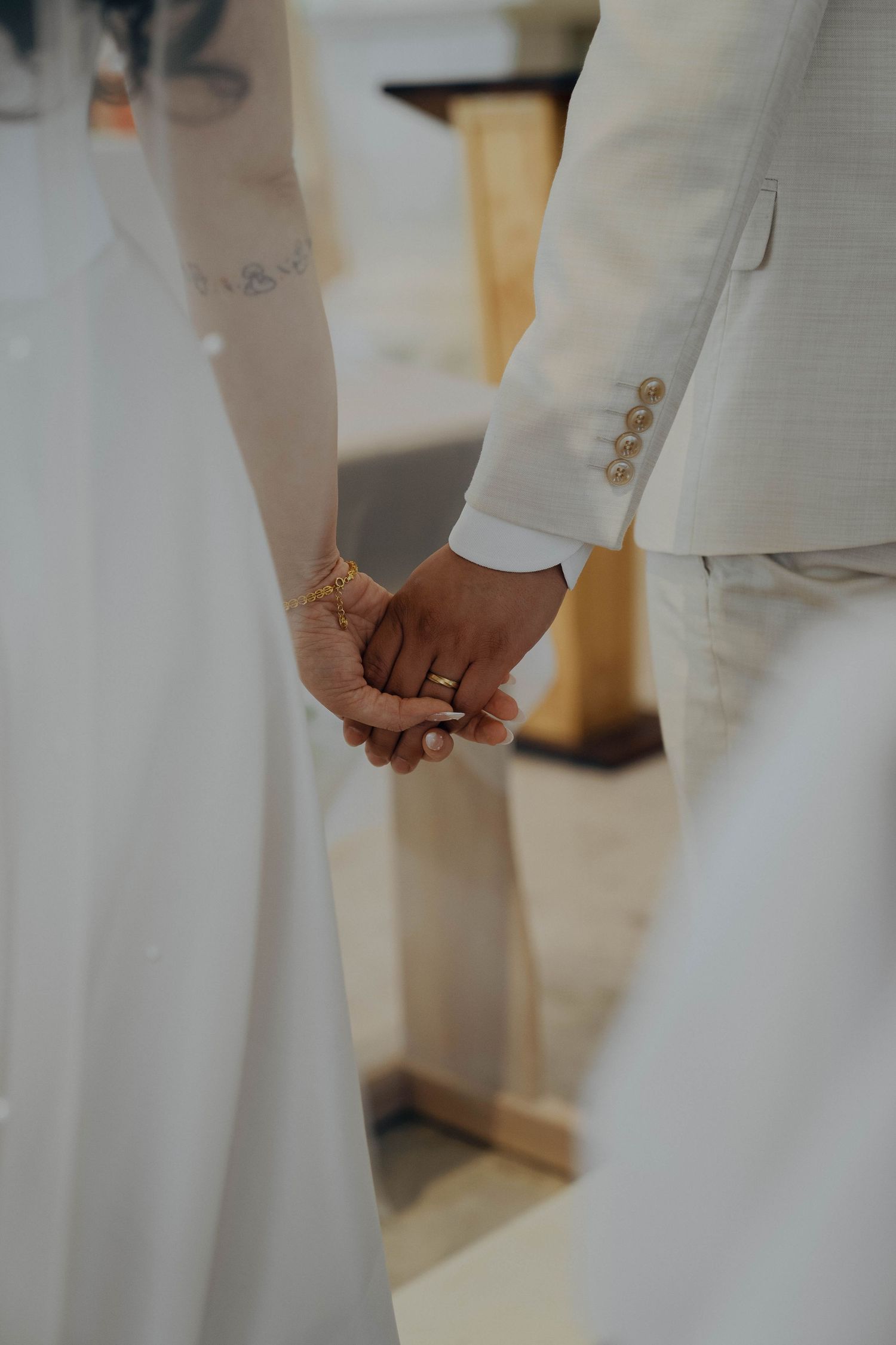 Close-up of a couple holding hands during their wedding ceremony, wearing white formal attire.