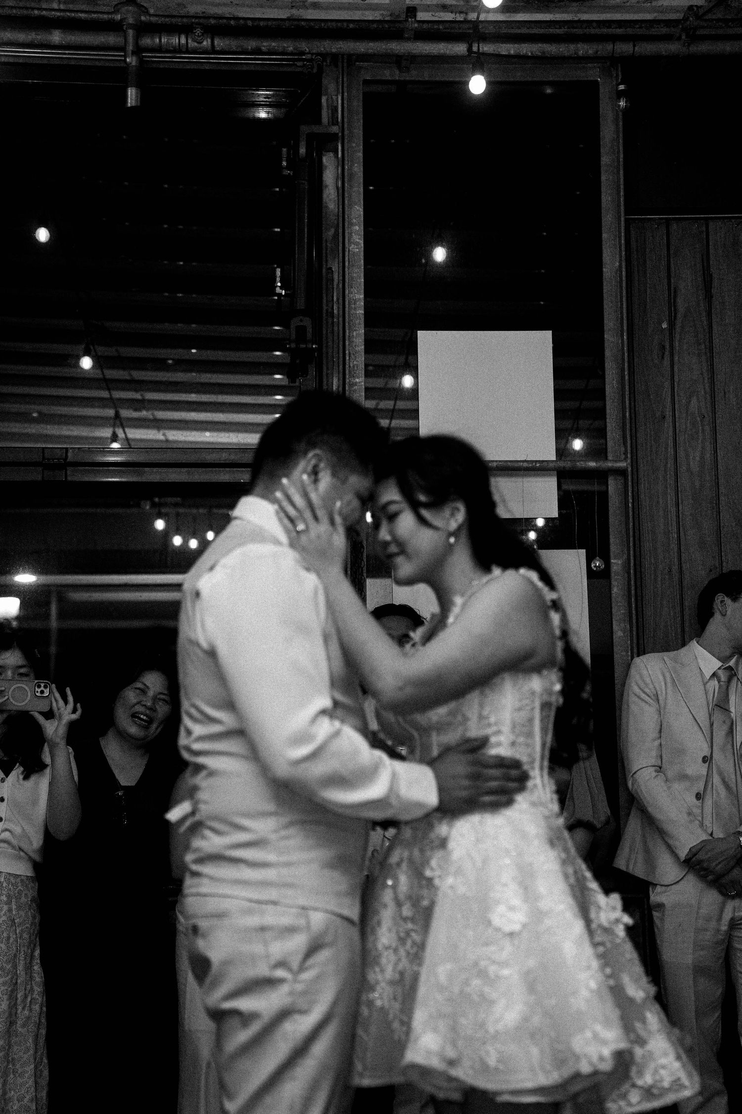 A romantic black and white photo of a couple sharing their first dance at a wedding reception with string lights glowing above.