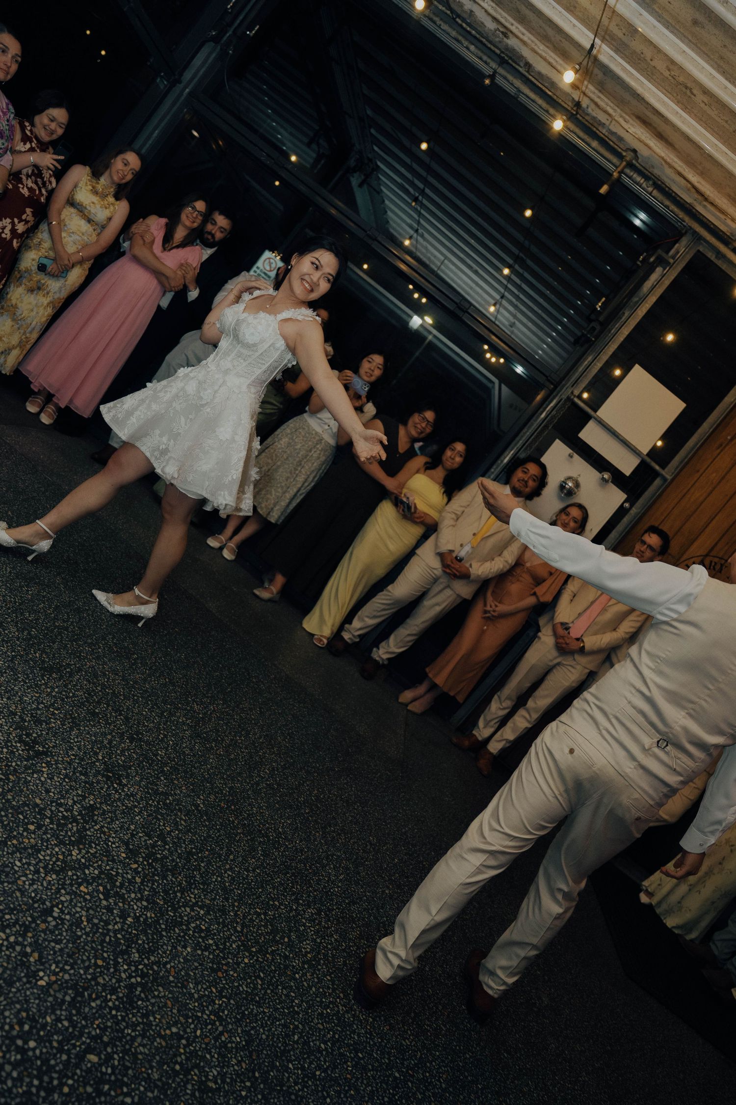 Wedding party guests line up on a dark floor for a fun dance line during an evening reception celebration.