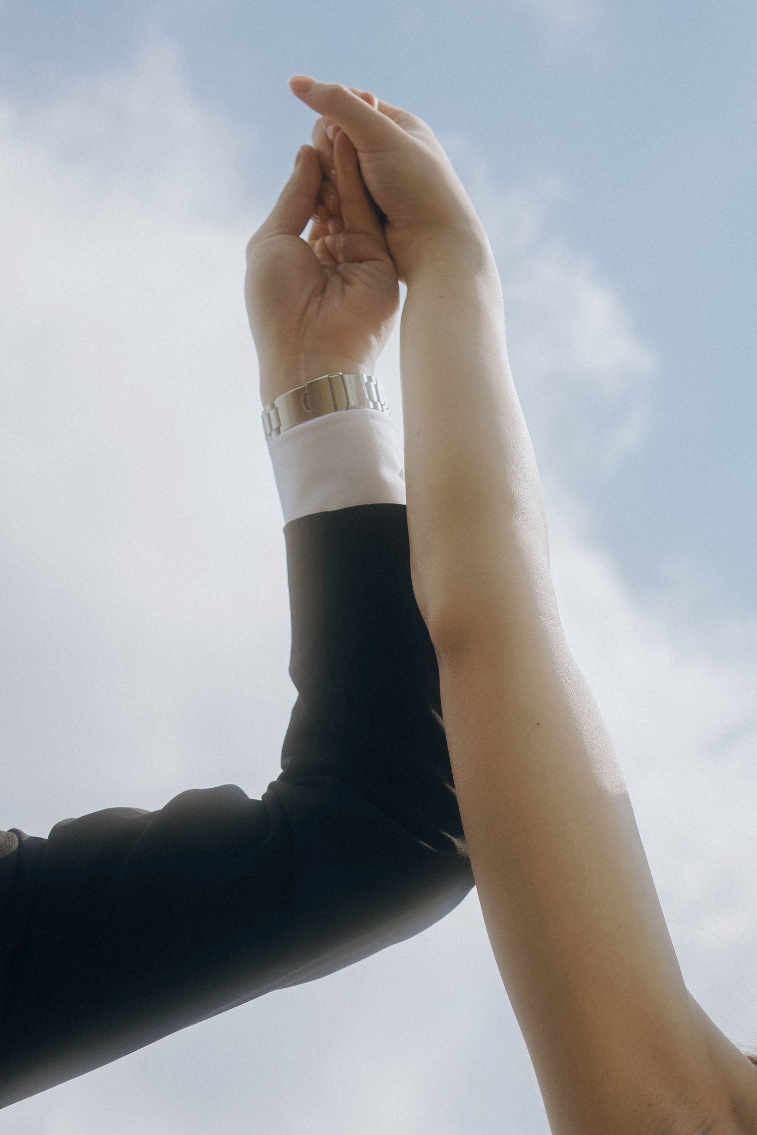 Two hands reaching upward against a cloudy sky, one wearing black and one in white, creating a contrasting silhouette.