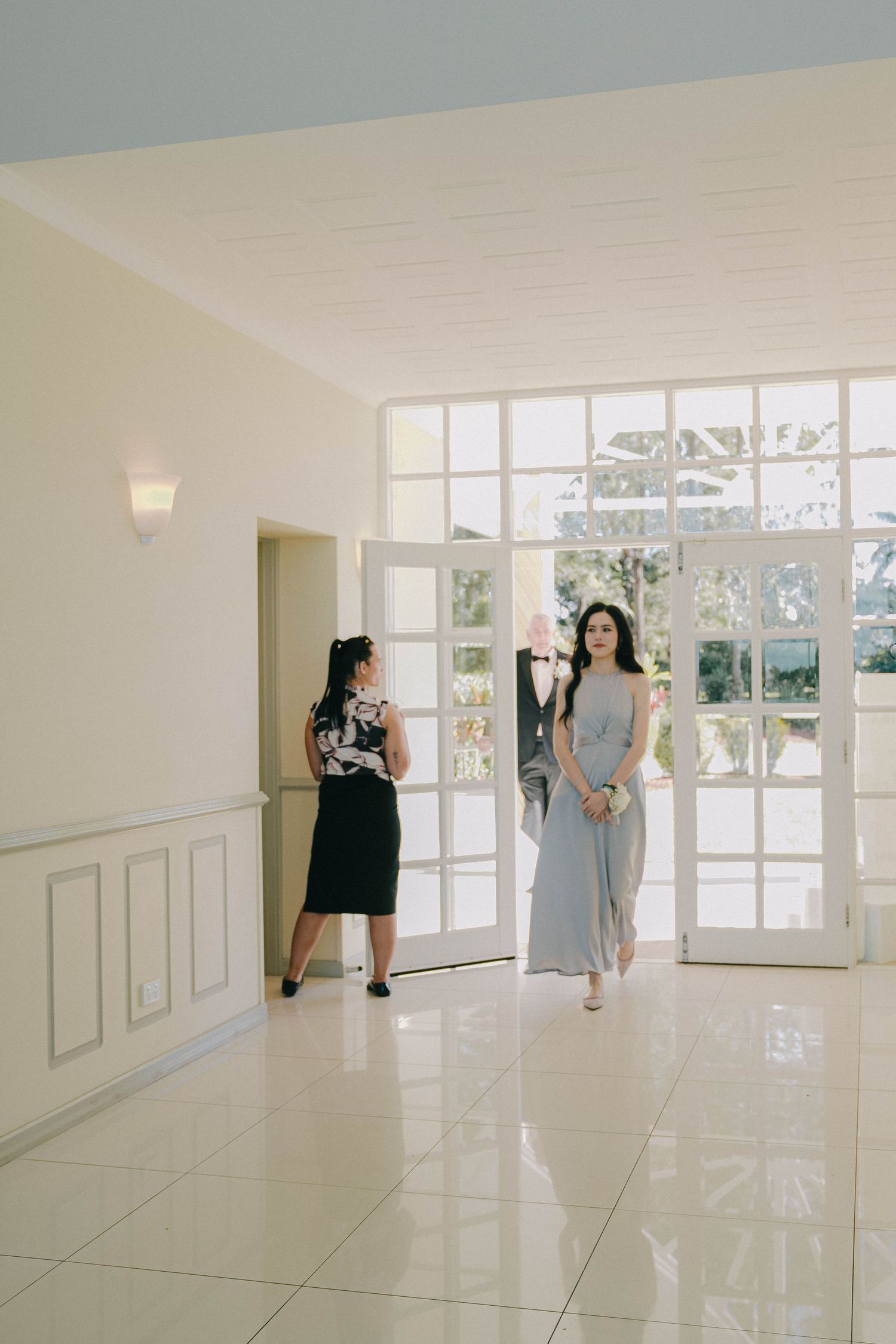 A sequence of dance poses captured in a bright, minimalist hallway with white walls and large windows.