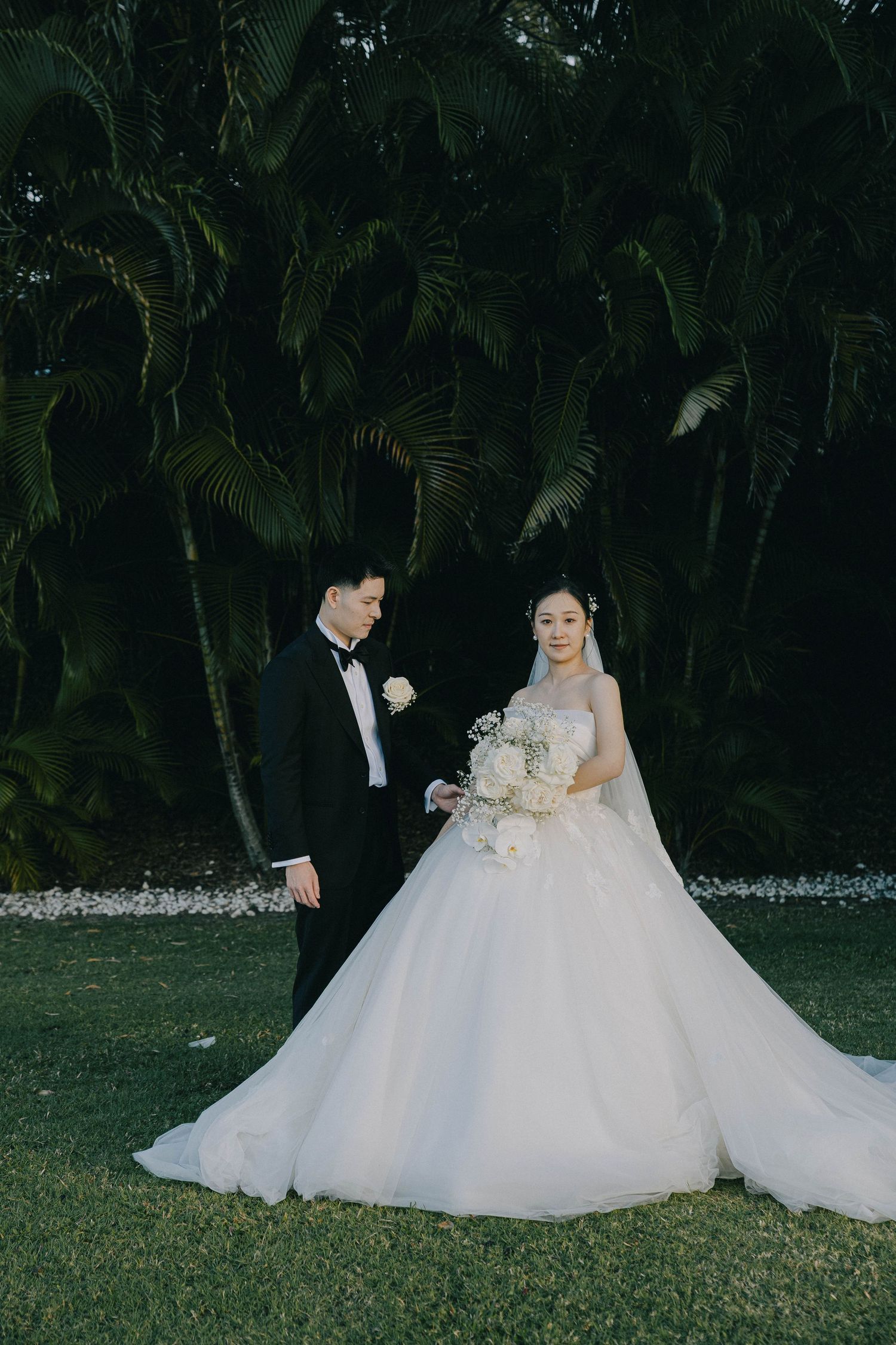 A couple poses together on their wedding day against a backdrop of lush tropical palm trees.