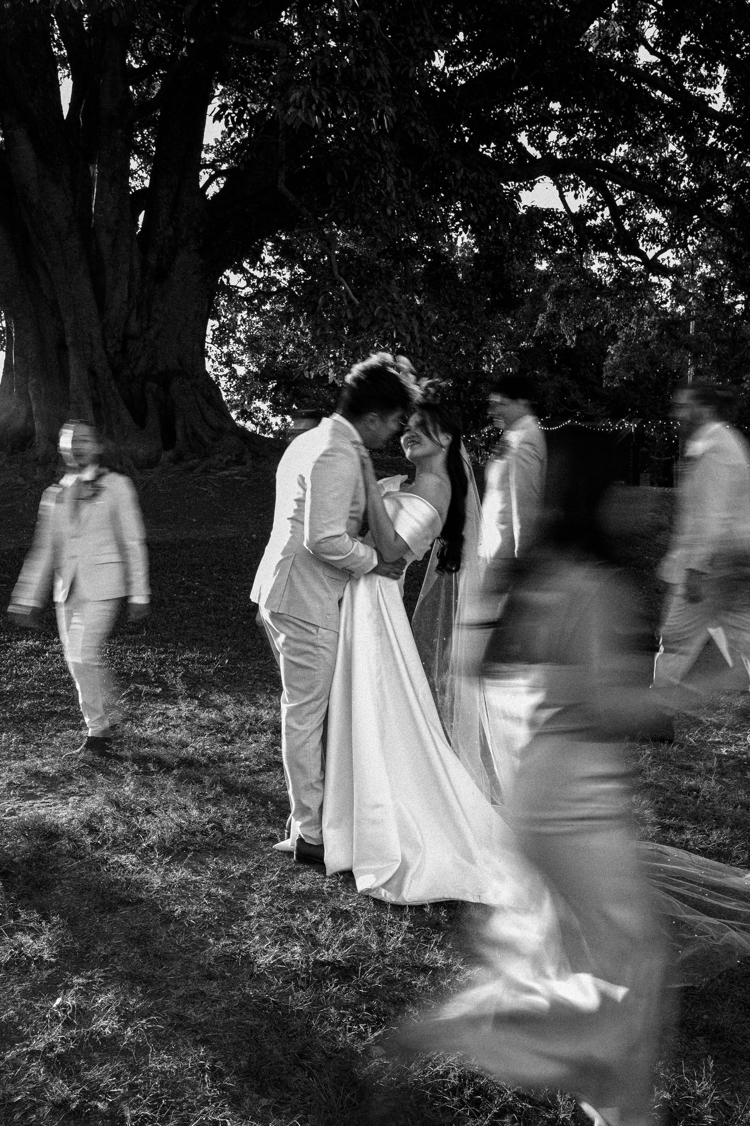 A sequence of black and white photos showing blurred figures walking in motion through a garden setting.
