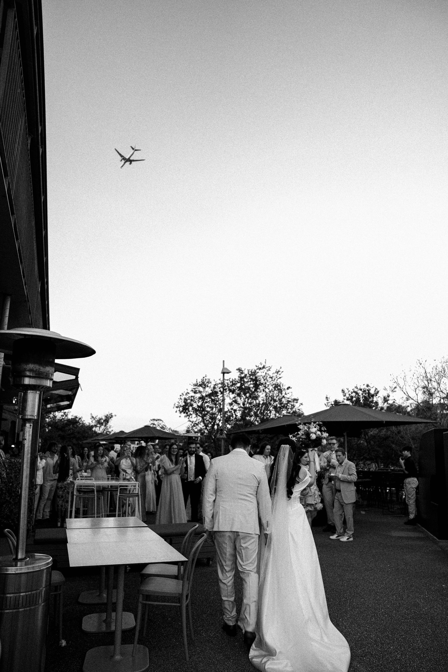 Black and white outdoor wedding ceremony setup with chairs arranged on grass and airplane flying overhead in background.