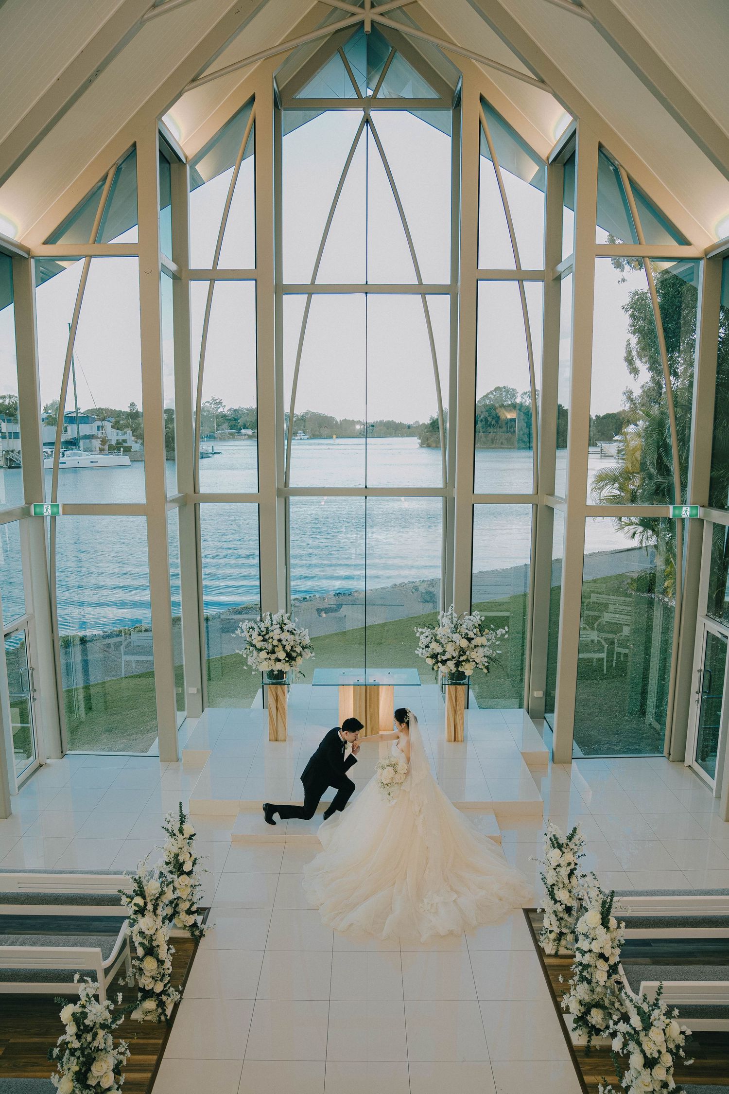 Elegant wedding chapel interior with white decor, floor-to-ceiling windows, and waterfront views.