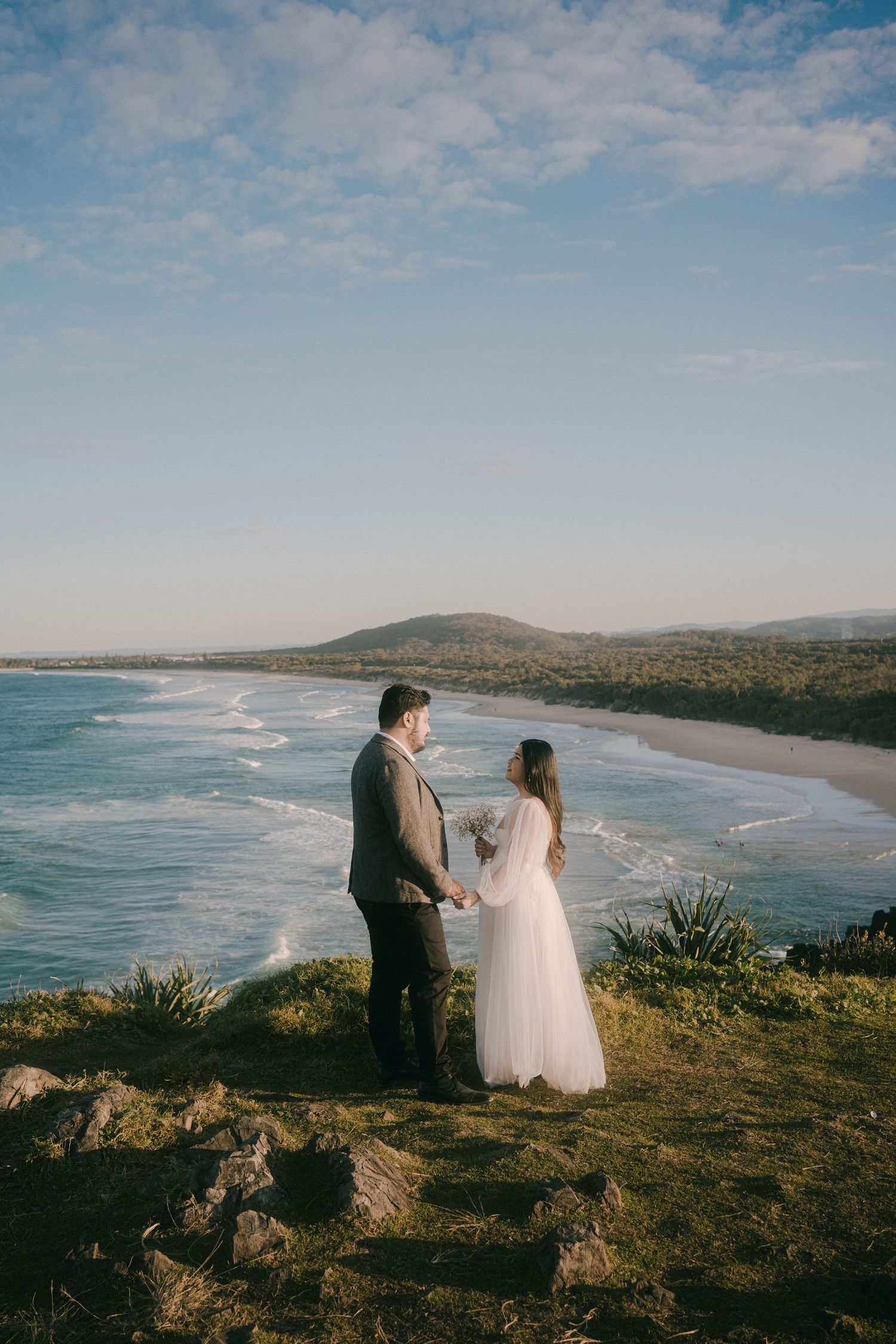 Scenic coastal wedding photography showing couple overlooking a beautiful beach landscape at sunset.