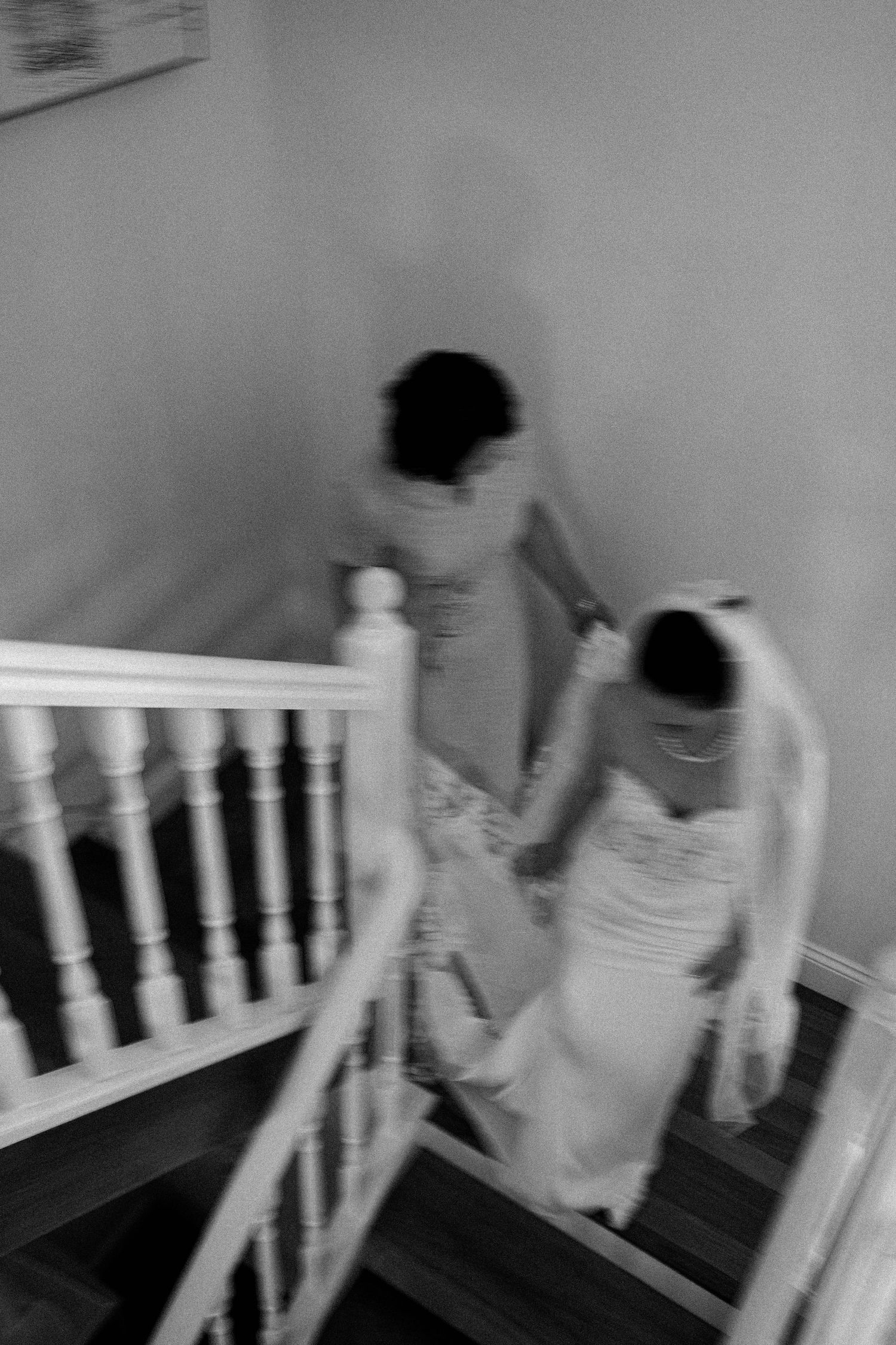 A blurry black and white photograph shows two people in formal attire descending a staircase with white railings.