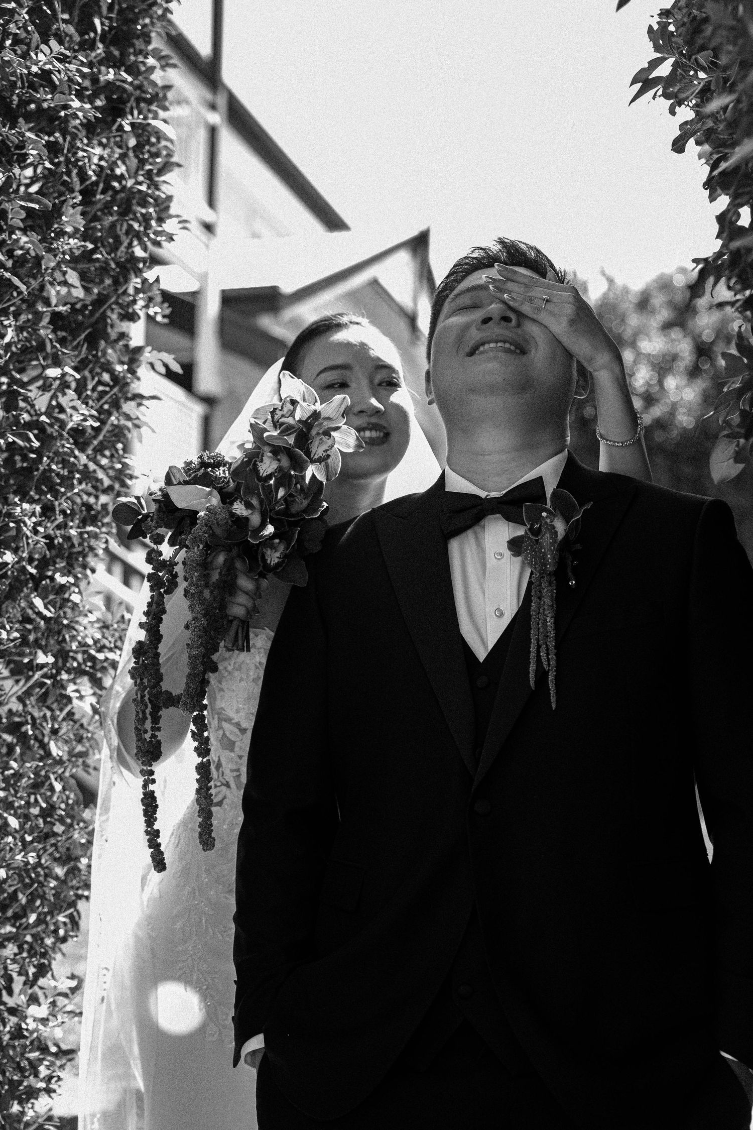 Black and white candid wedding photo showing joyful laughter during an outdoor ceremony under natural lighting.