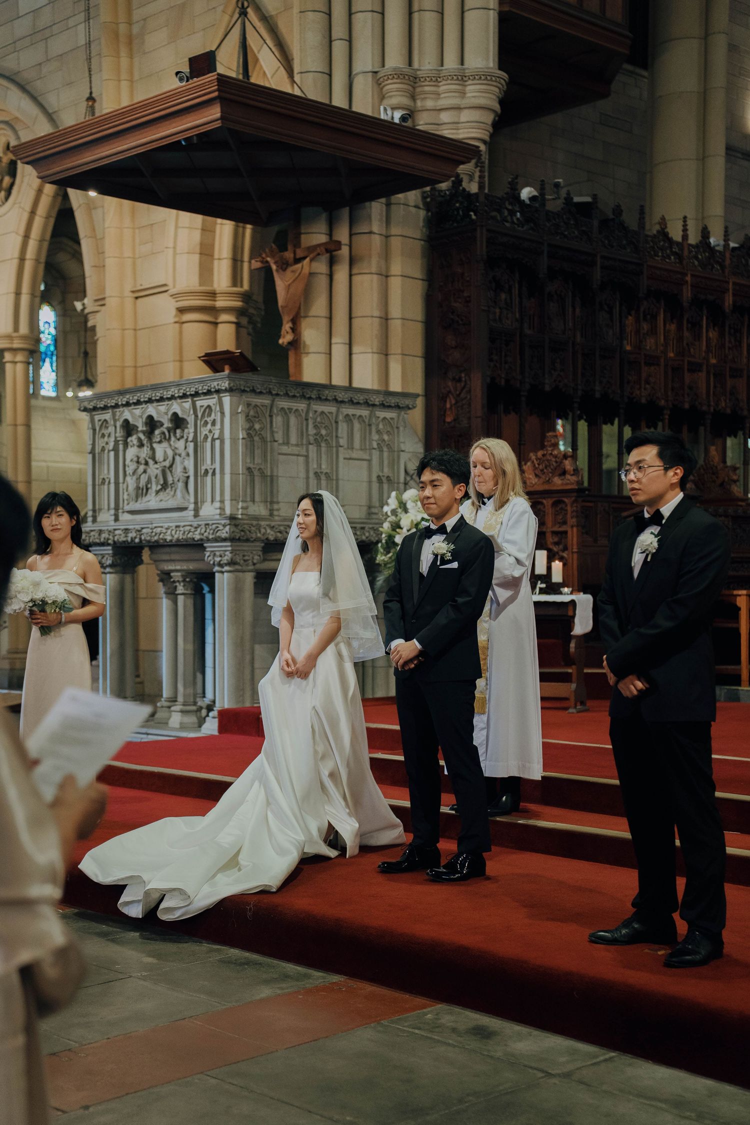 A wedding ceremony takes place in a grand cathedral with ornate architecture and red carpeted aisle.