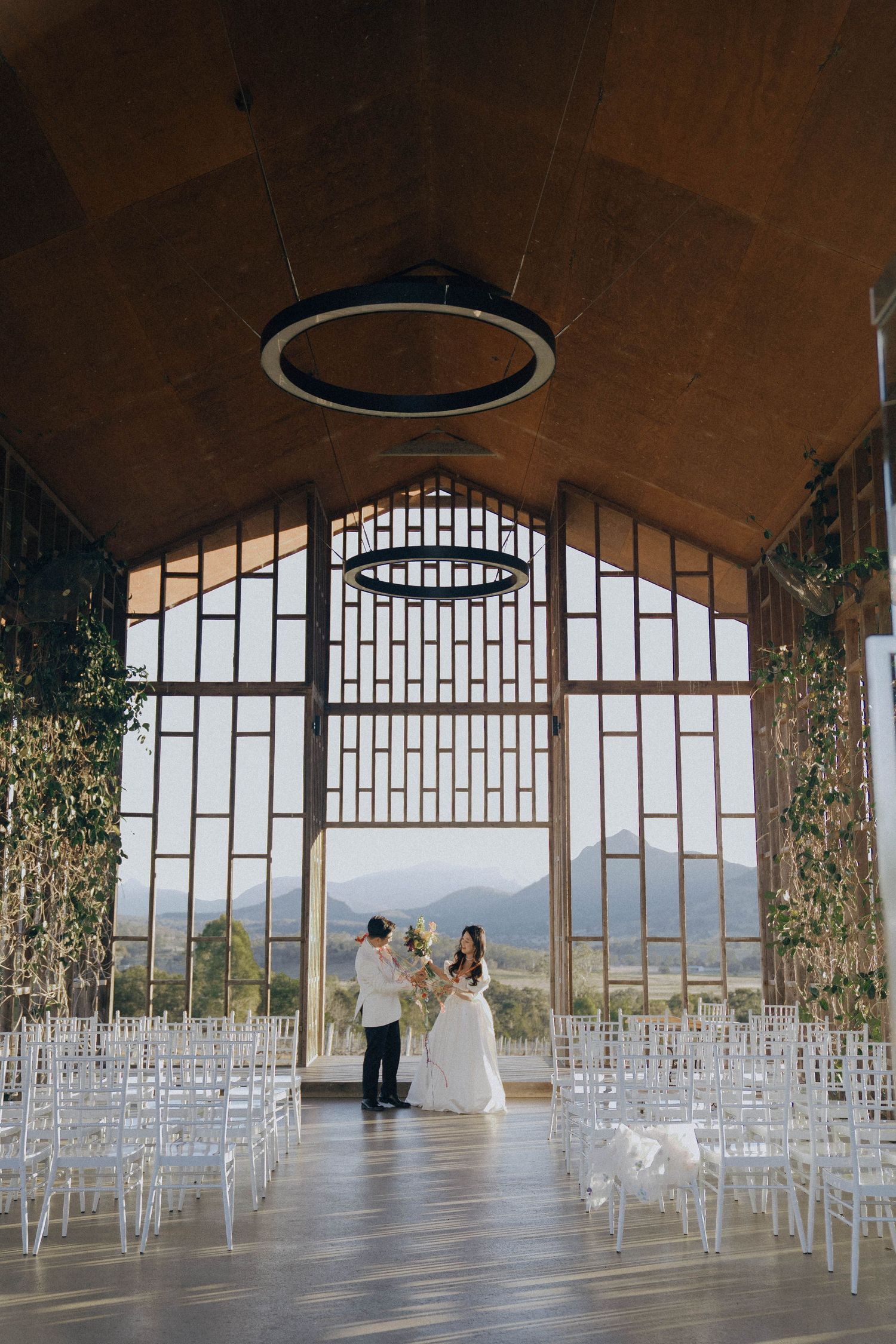 Modern wedding ceremony setup inside a curved architectural space with mountain views through large arched windows.