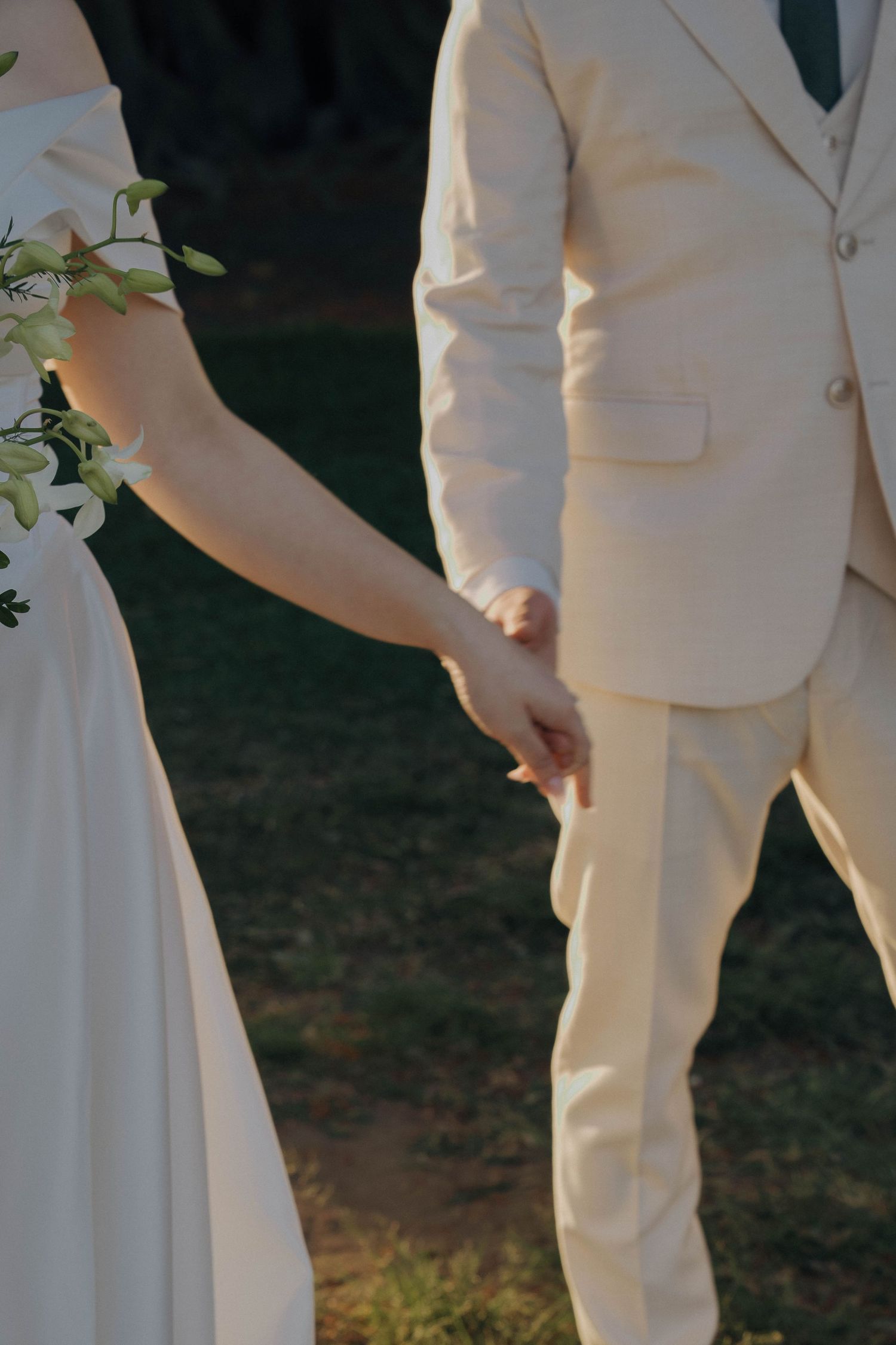 Close-up view of wedding party members in cream-colored suits and white dresses standing together outdoors.