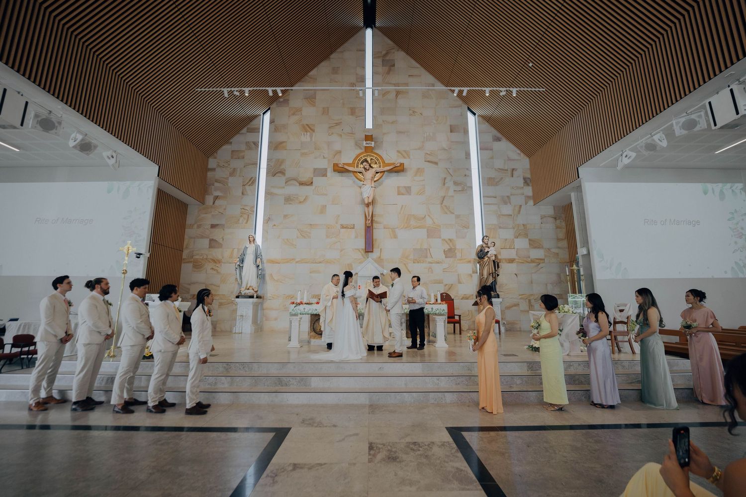 People in white robes stand in line during a religious ceremony at a church altar with crosses and candles.