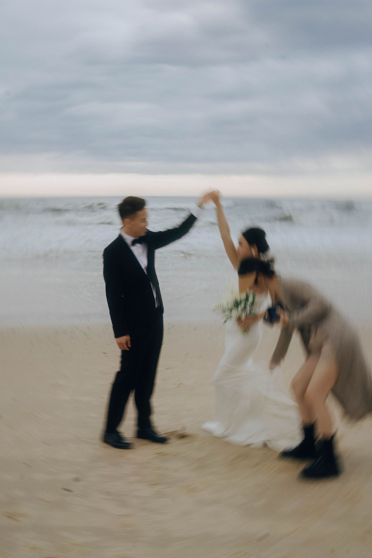 Two people in motion on a misty beach creating a dynamic, blurred dance-like sequence against an overcast sky.